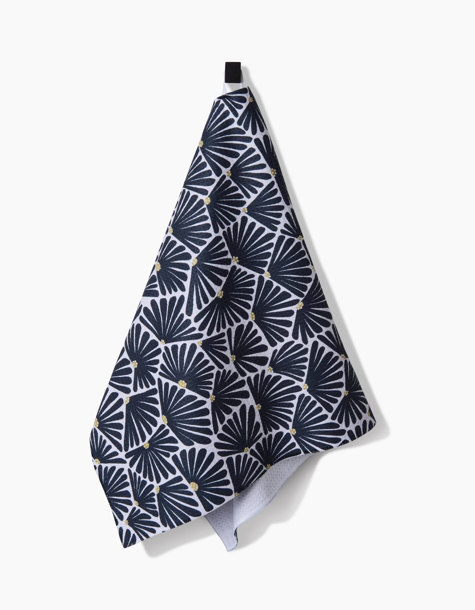 The Solie Black Tea Towel by Amy MacCready, featuring a black and white geometric fan pattern with small yellow dots and made from ultra-absorbent Geoweave™ fabric, hangs from a black loop against a plain white background.
