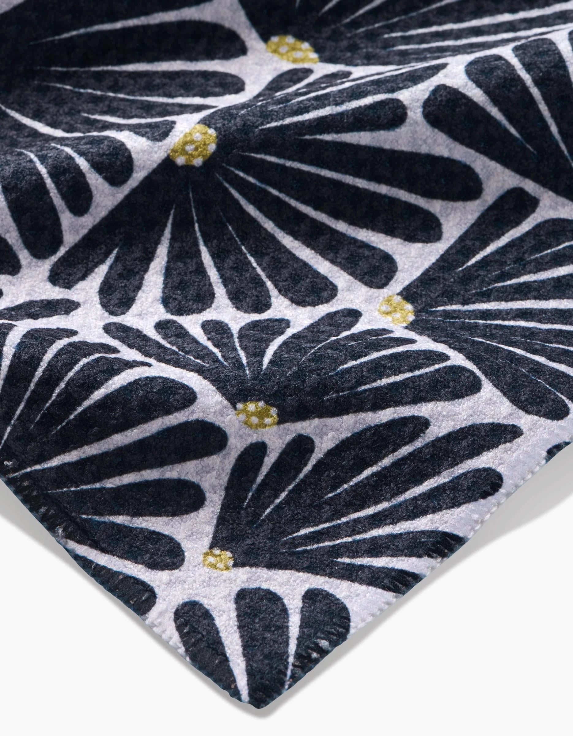 A close-up of an Amy MacCready Solie Black Tea Towel shows ultra-absorbent Geoweave™ fabric with a repeating navy blue floral pattern and small yellow centers on a light grey background, neatly stitched along the edge.