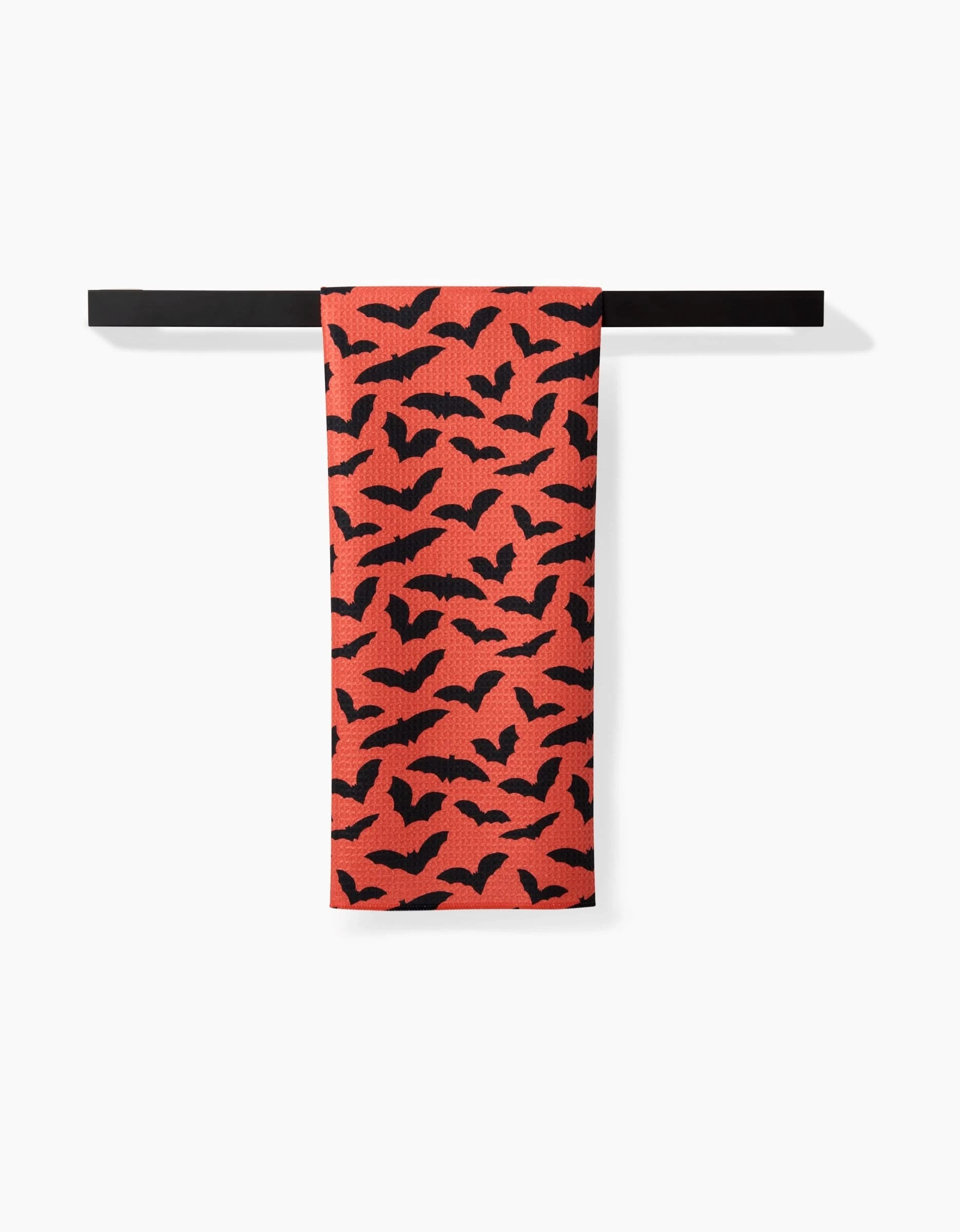 The Rebecca Bobko Spooky Bats tea towel features black bats scattered across its red fabric and hangs from a black rod.