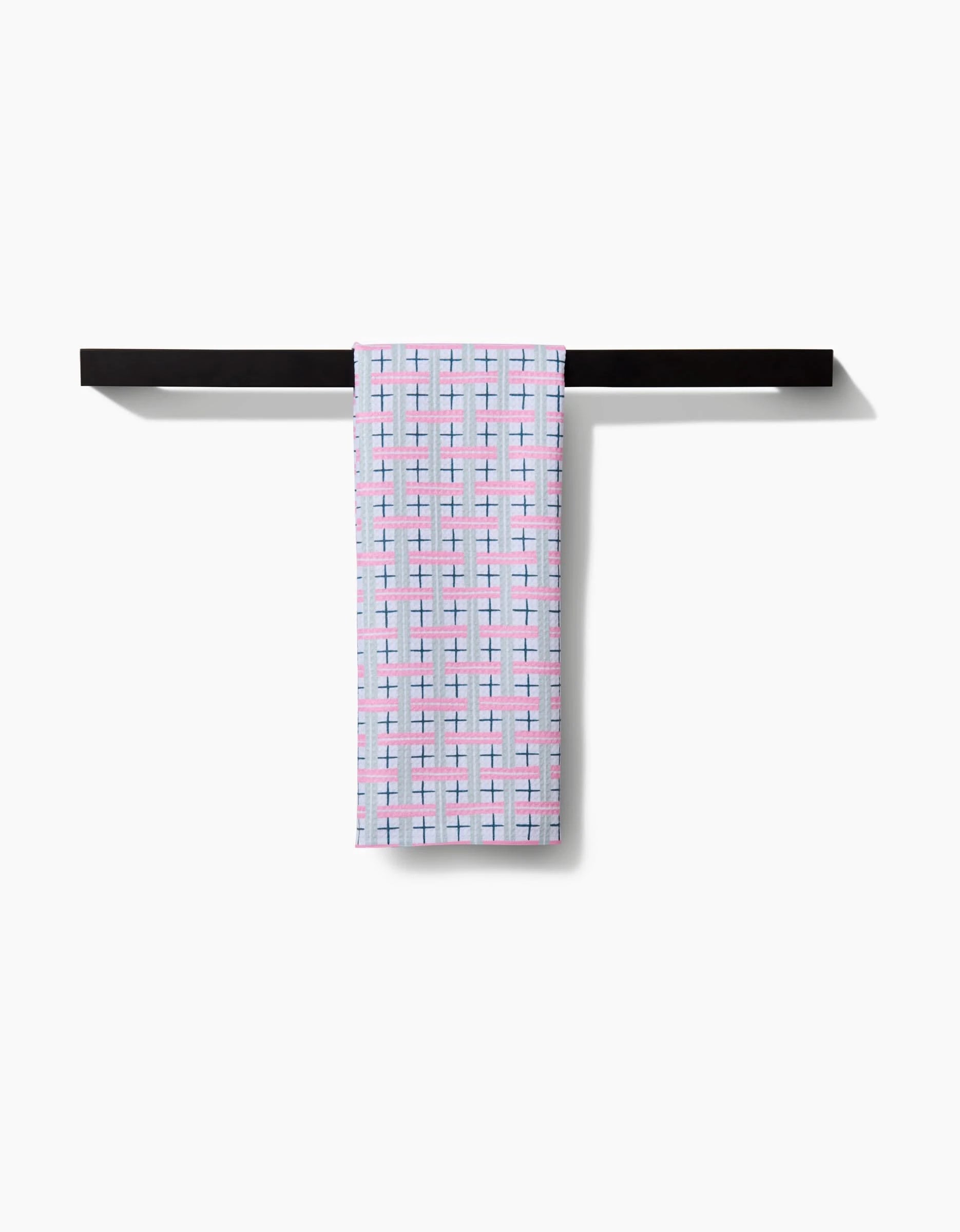 A folded Hufton Studio Spring Cottage Plaid Tea Towel with a blue, pink, and black grid pattern hangs neatly over a sleek black towel bar against a white background.