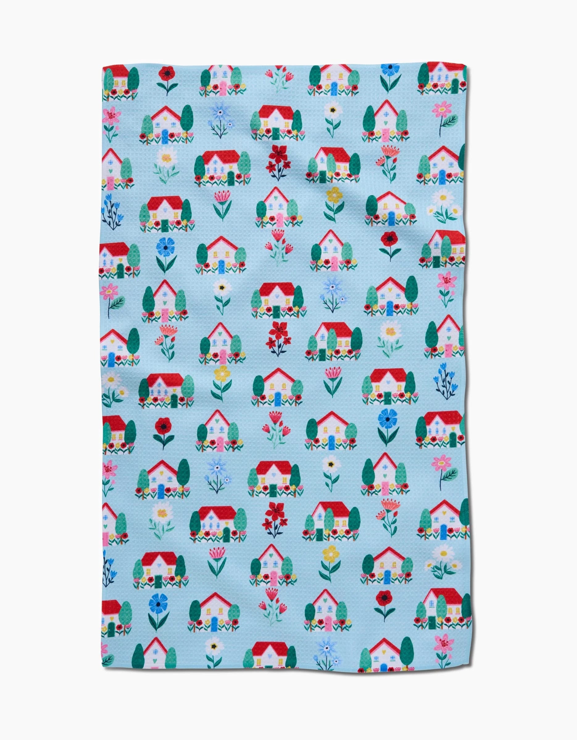 The Spring Houses blanket by Ceyda Alasar is light blue with a colorful pattern of houses, trees, and flowers in red, pink, blue, and green. Made from recycled materials for an eco-friendly touch.
