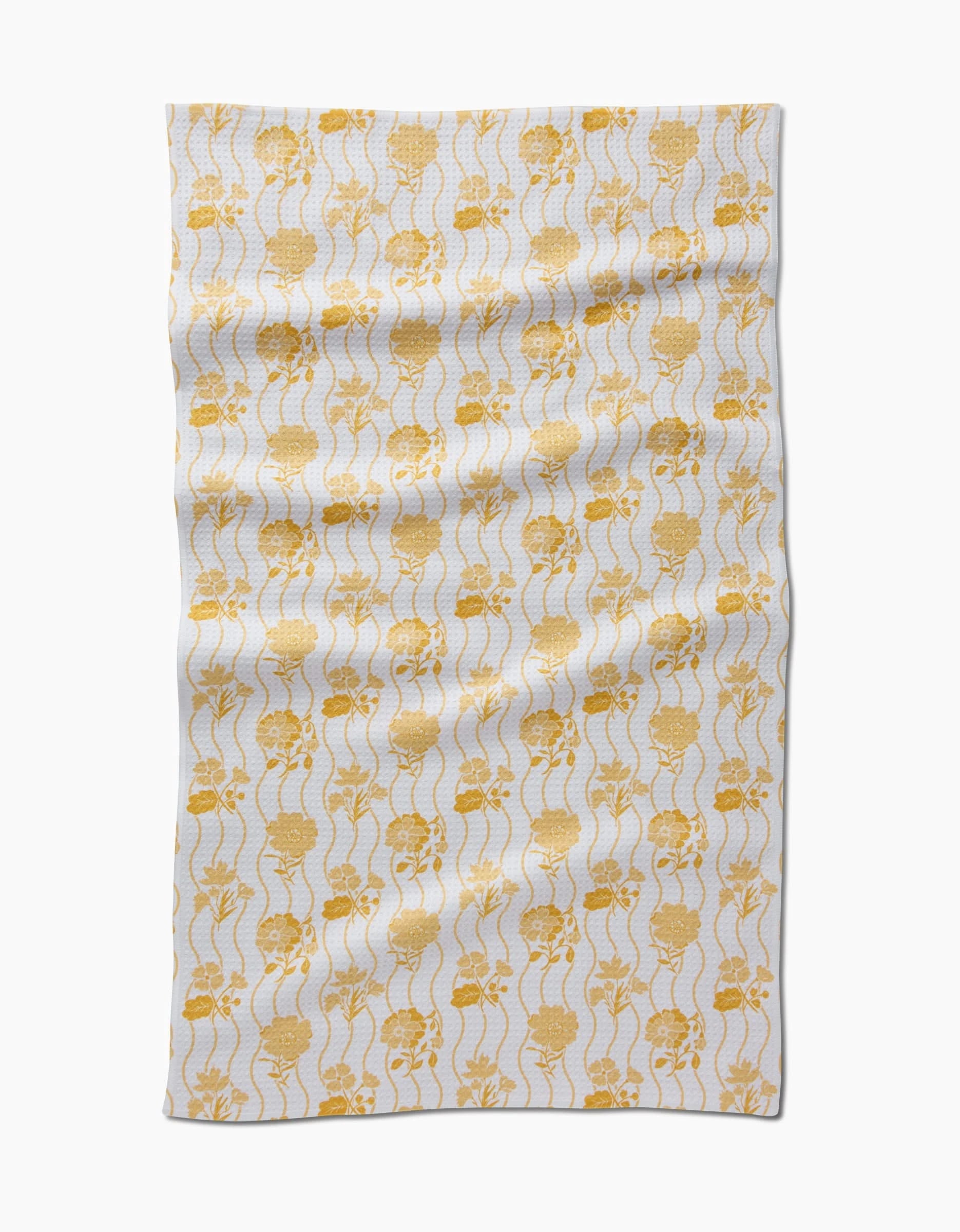 The Spring Wave tea towel by Danelys Sidron features yellow skulls and wavy vertical lines on soft Geoweave fabric. Its rectangular, white design is shown slightly wrinkled against a plain white background.