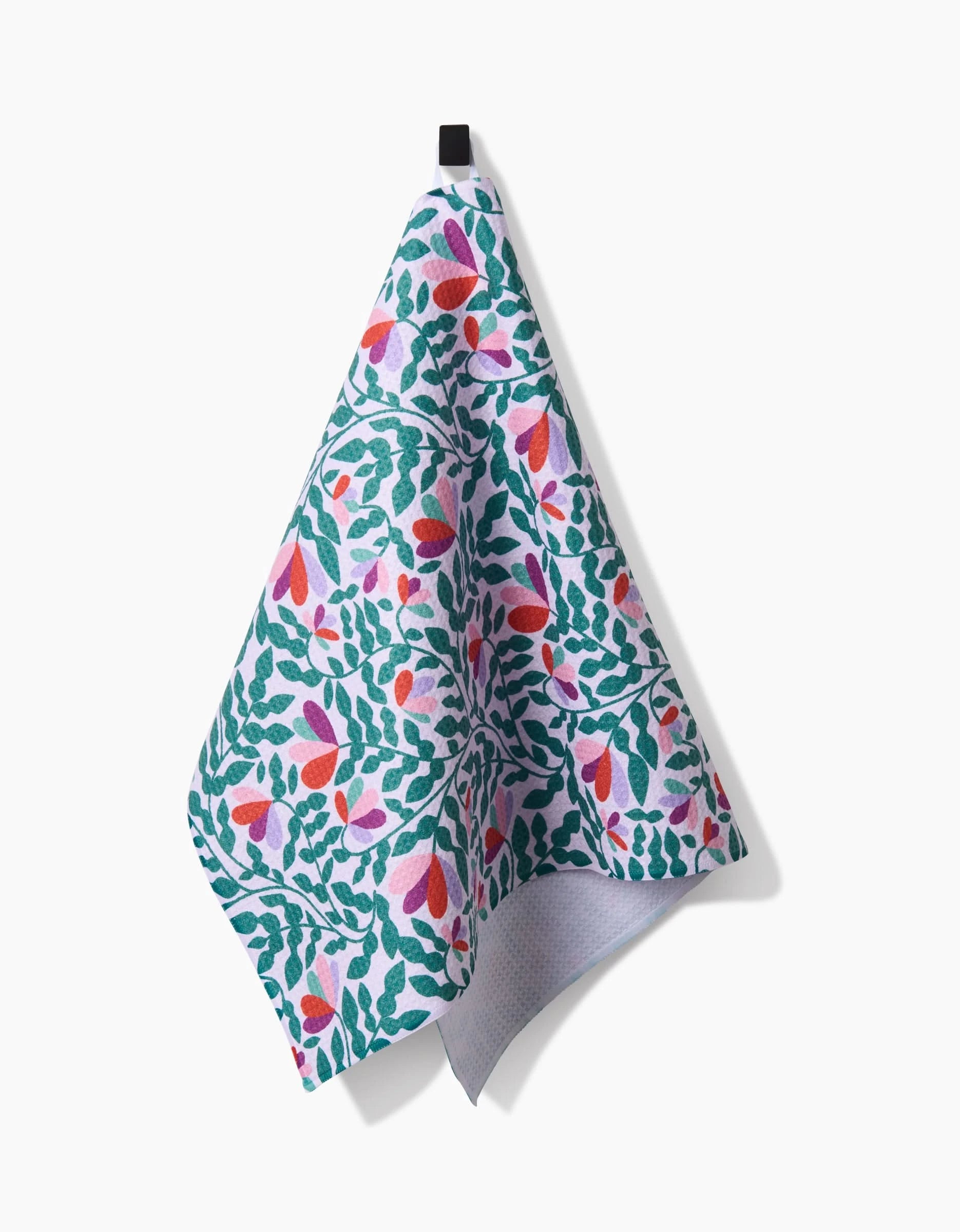 The Claire Iglesias “Spring Wavy Leaves” Tea Towel, featuring a green, pink, and red floral and leafy pattern on Geoweave fabric, hangs by a black loop against a white background.