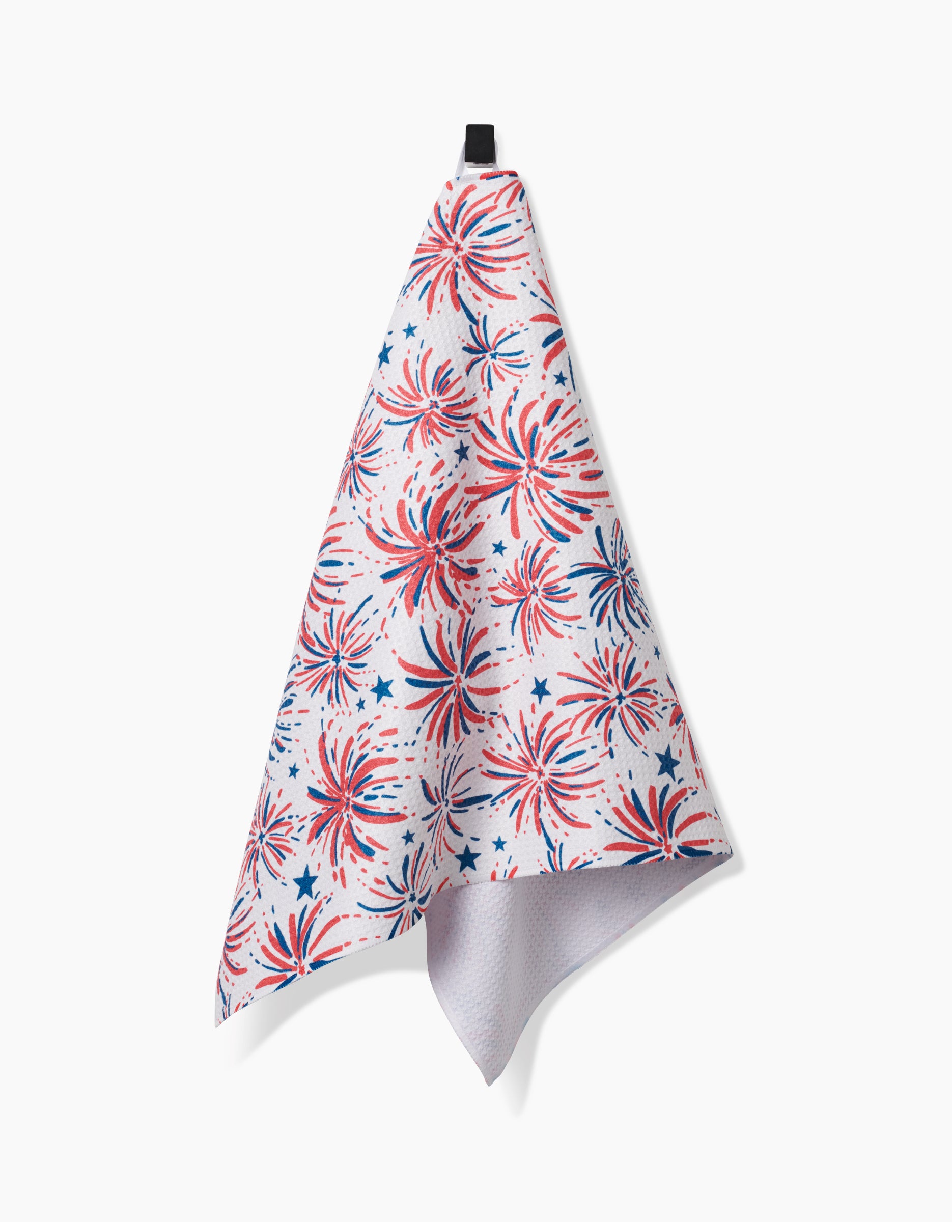 The Hufton Studio Stars And Fireworks white tea towel hangs from a black loop, featuring red, white, and blue fireworks and stars on Geoweave fabric for a festive patriotic touch.