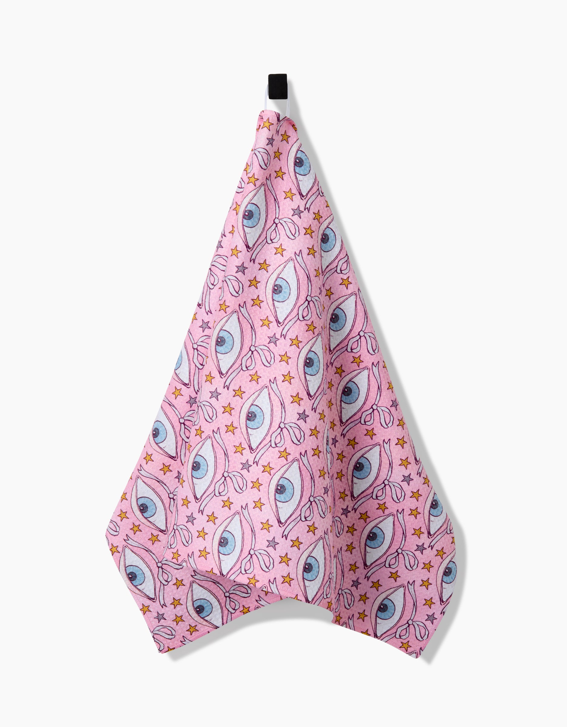 The Stella tea towel by Maayan Alper-Swan features pink Geoweave fabric with blue eyes, stars, and orange dots in a repeating pattern, hanging from a black loop against a white background.