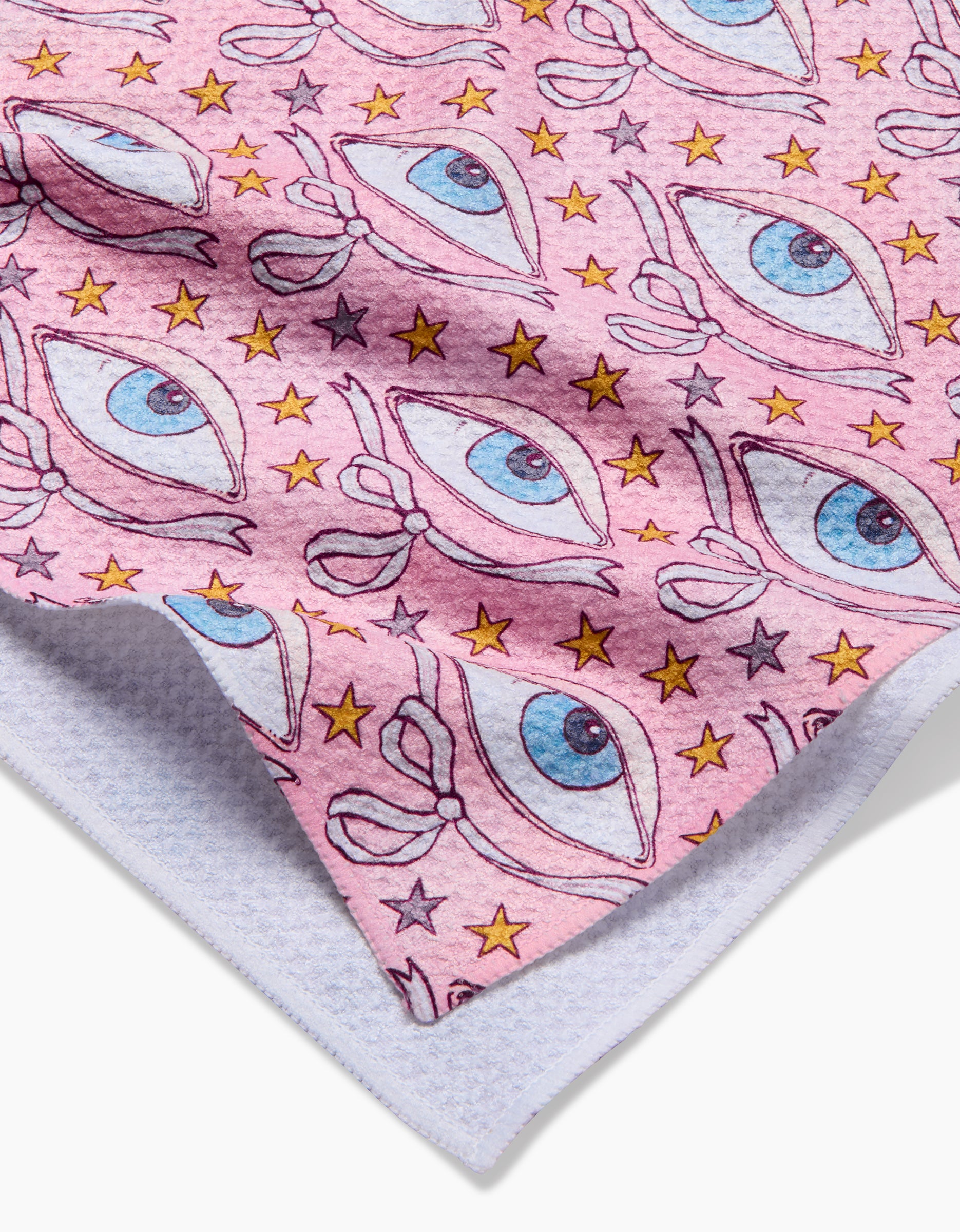 A close-up of Maayan Alper-Swan’s Stella tea towel shows pink Geoweave fabric with a blue eye and yellow star pattern. The towel is slightly folded, revealing its textured white underside made from recycled materials.