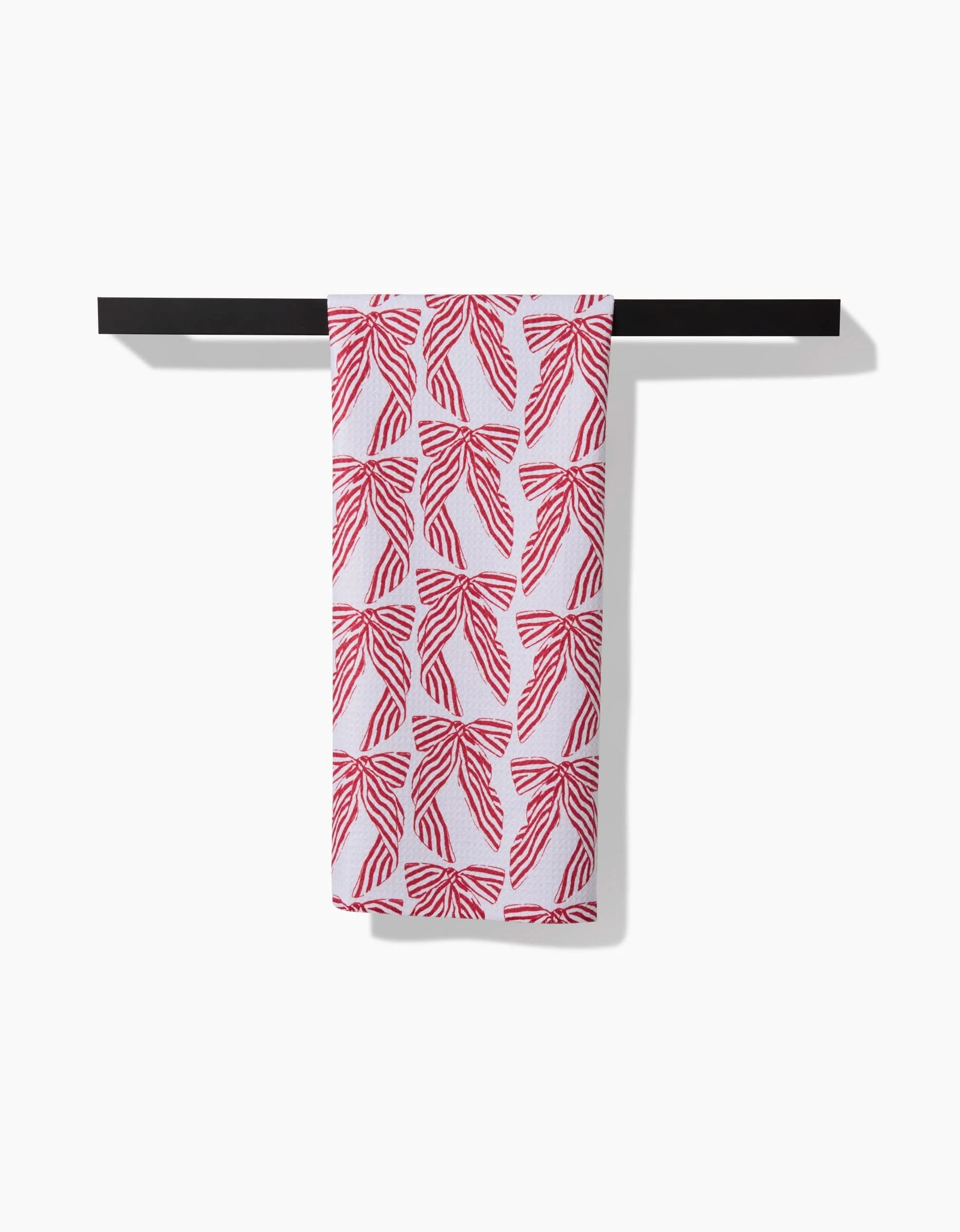 The Hufton Studio Striped Bows tea towel, featuring a repeating red abstract pattern, hangs neatly over a horizontal black towel bar against a plain white background.