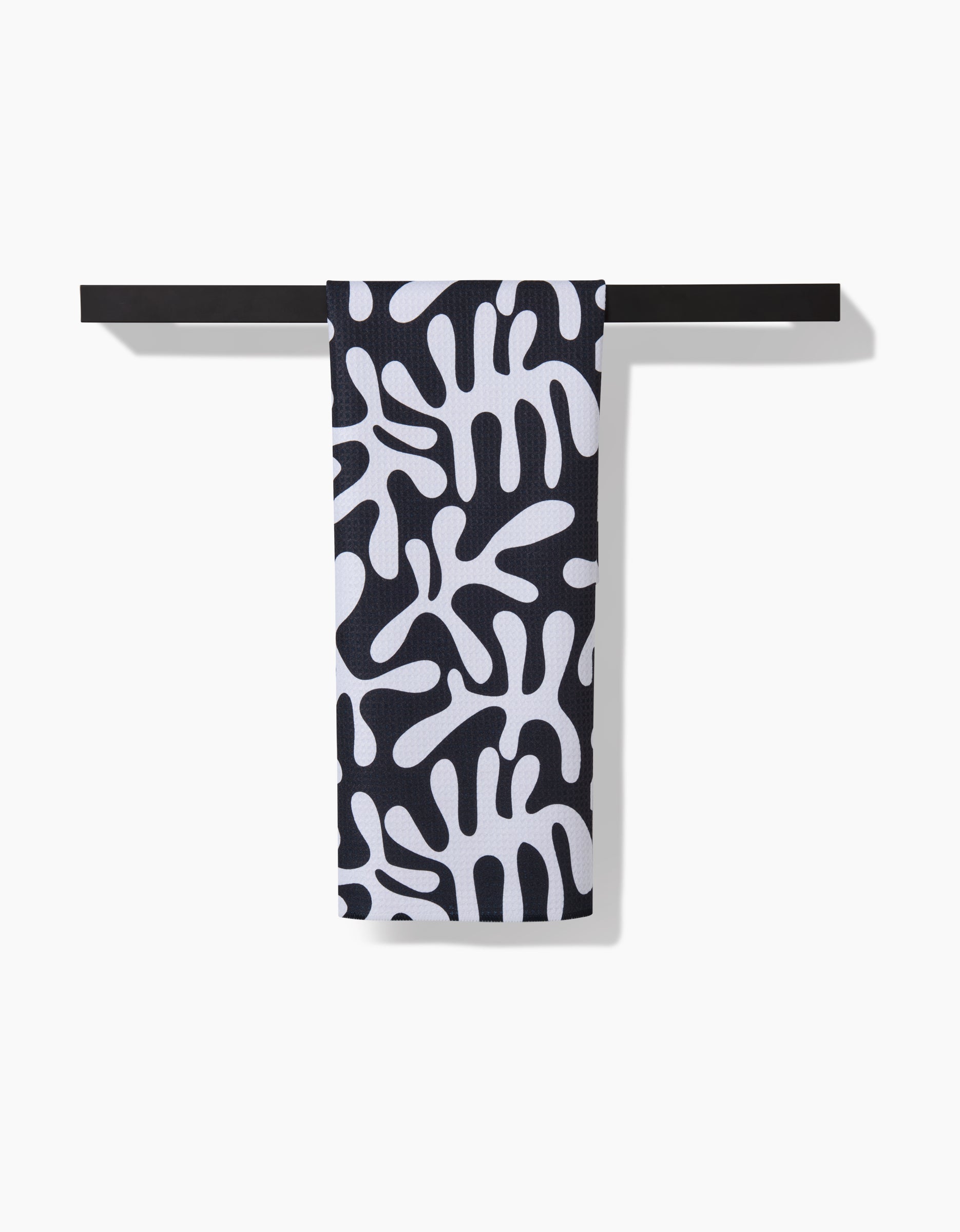 A Marina Solodka Sunset tea towel in ultra-absorbent Geoweave™ fabric, displaying an abstract white organic pattern, hangs neatly on a black towel bar against a white background.