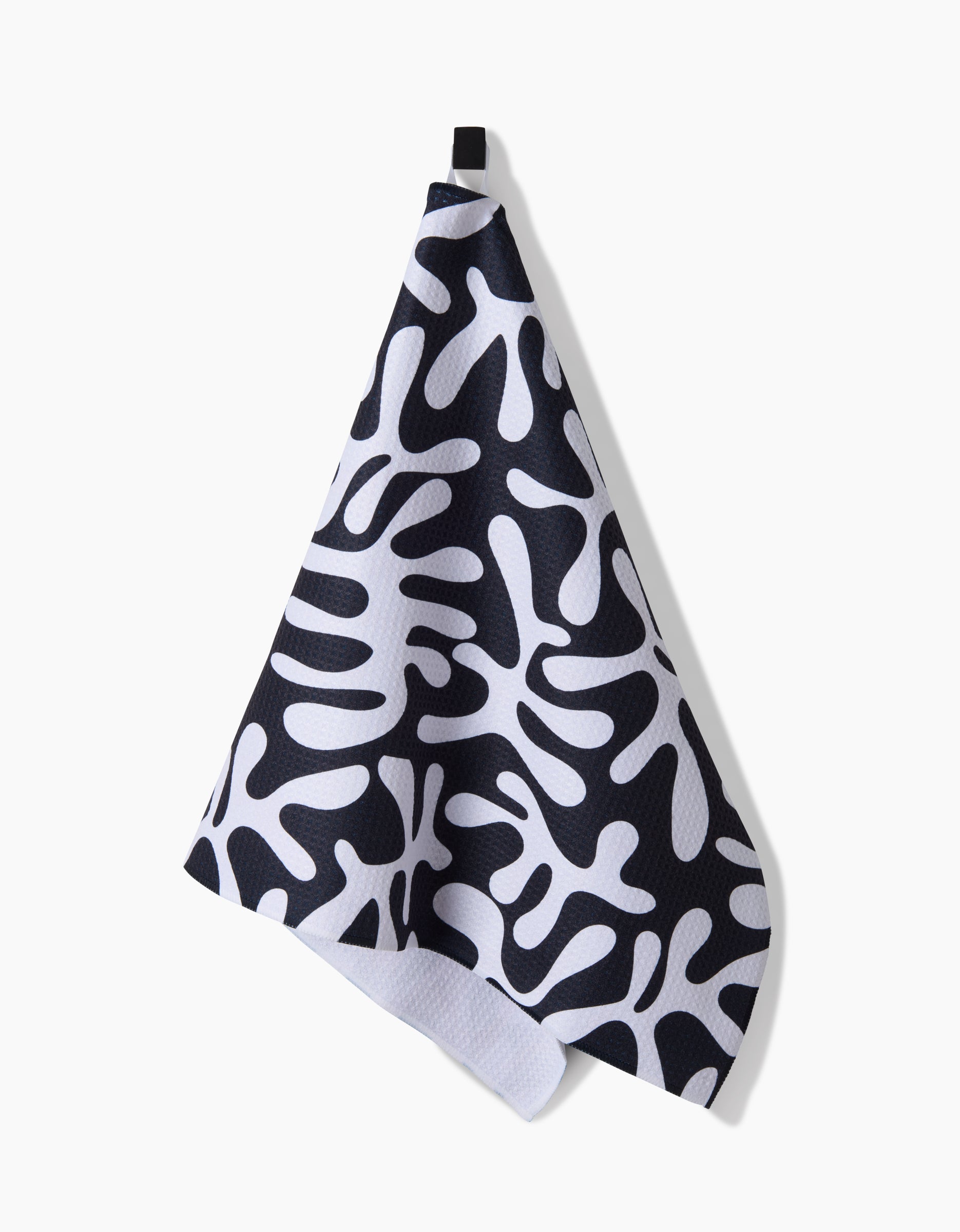 The Sunset tea towel by Marina Solodka features a bold, abstract black pattern on white and hangs from a black loop. Made from ultra-absorbent Geoweave™ fabric for exceptional performance, it brightens any kitchen setting.