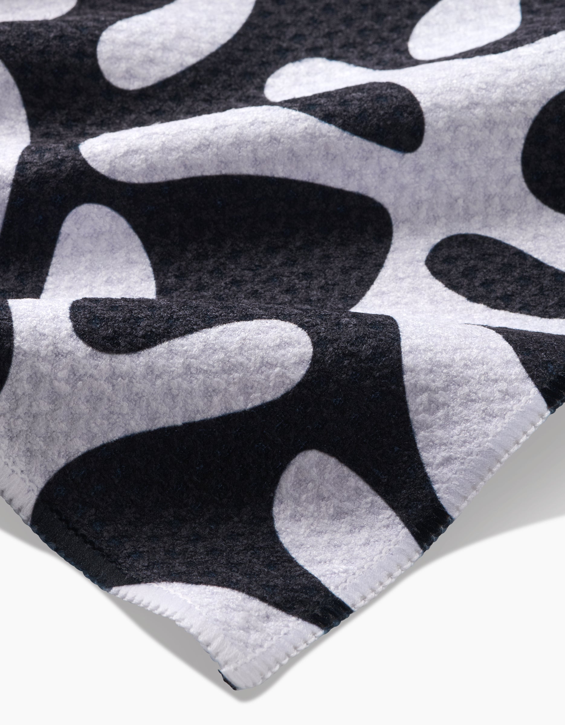 A close-up of the Marina Solodka Sunset Tea Towel, made from Geoweave™ fabric, features a black and white abstract organic pattern with a textured ultra-absorbent surface and stitched edges.