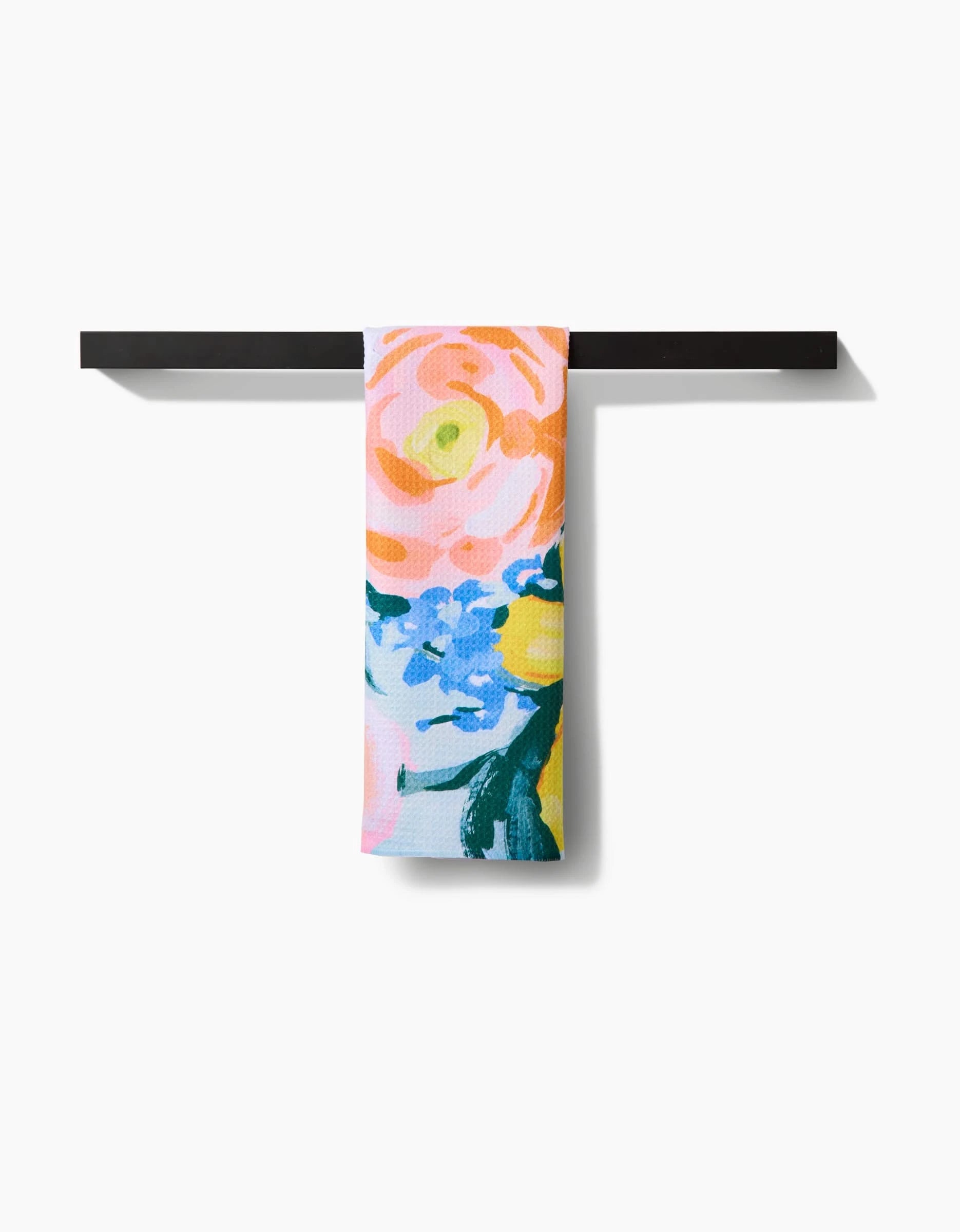 The Suzzy tea towel by Ania Zwara Art features a vibrant pink, orange, and blue floral design on durable Geoweave fabric, displayed neatly over a black bar with a white background.