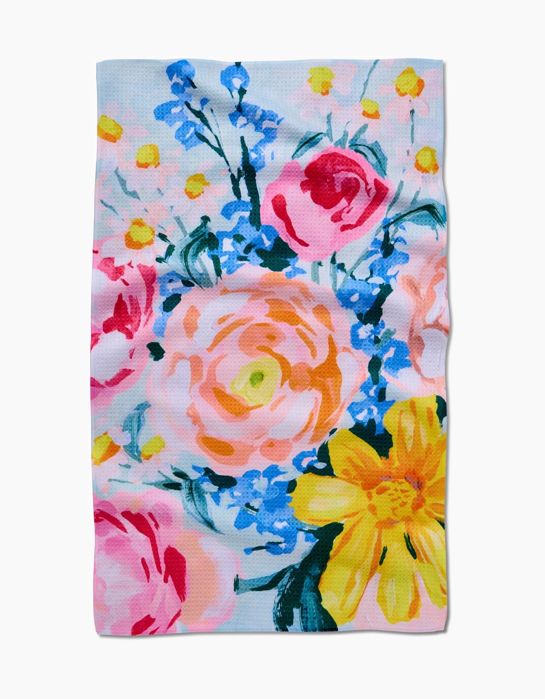 The Suzzy tea towel by Ania Zwara Art features a vibrant floral pattern with pink roses, yellow daisy-like blooms, and blue accents on a light background, crafted from soft Geoweave fabric.