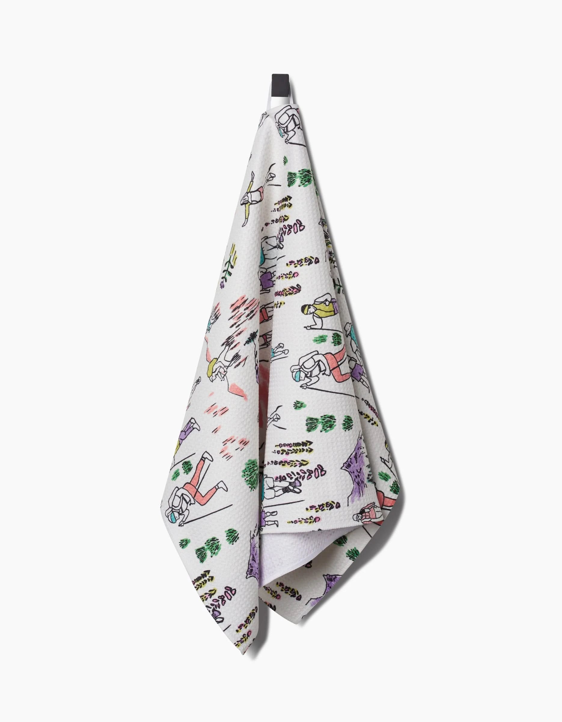 The Take A Hike tea towel by Elisabeth Wing is made from durable Geoweave fabric and hangs from a black loop. It features playful, colorful illustrations of people, trees, and outdoor activities on a white textured background.