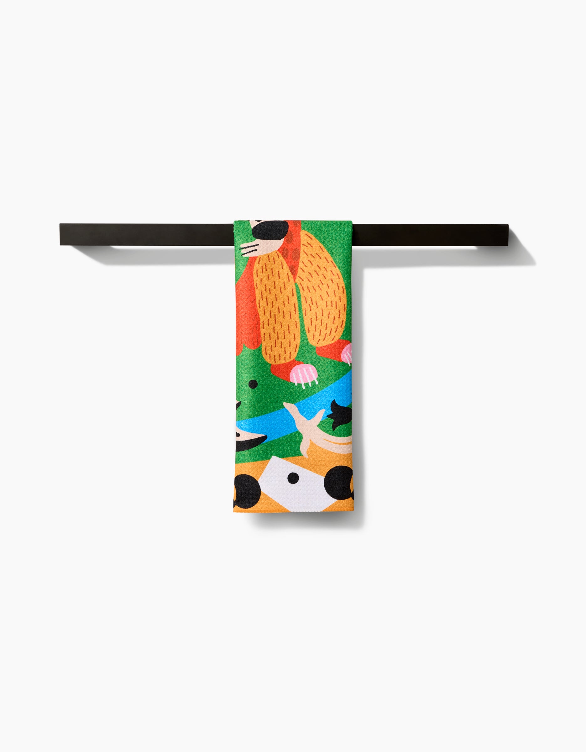 The Tamanduá Bandeira tea towel by Camila Leão, featuring playful animal illustrations, is made from recycled materials and displayed folded over a black towel bar against a white background.