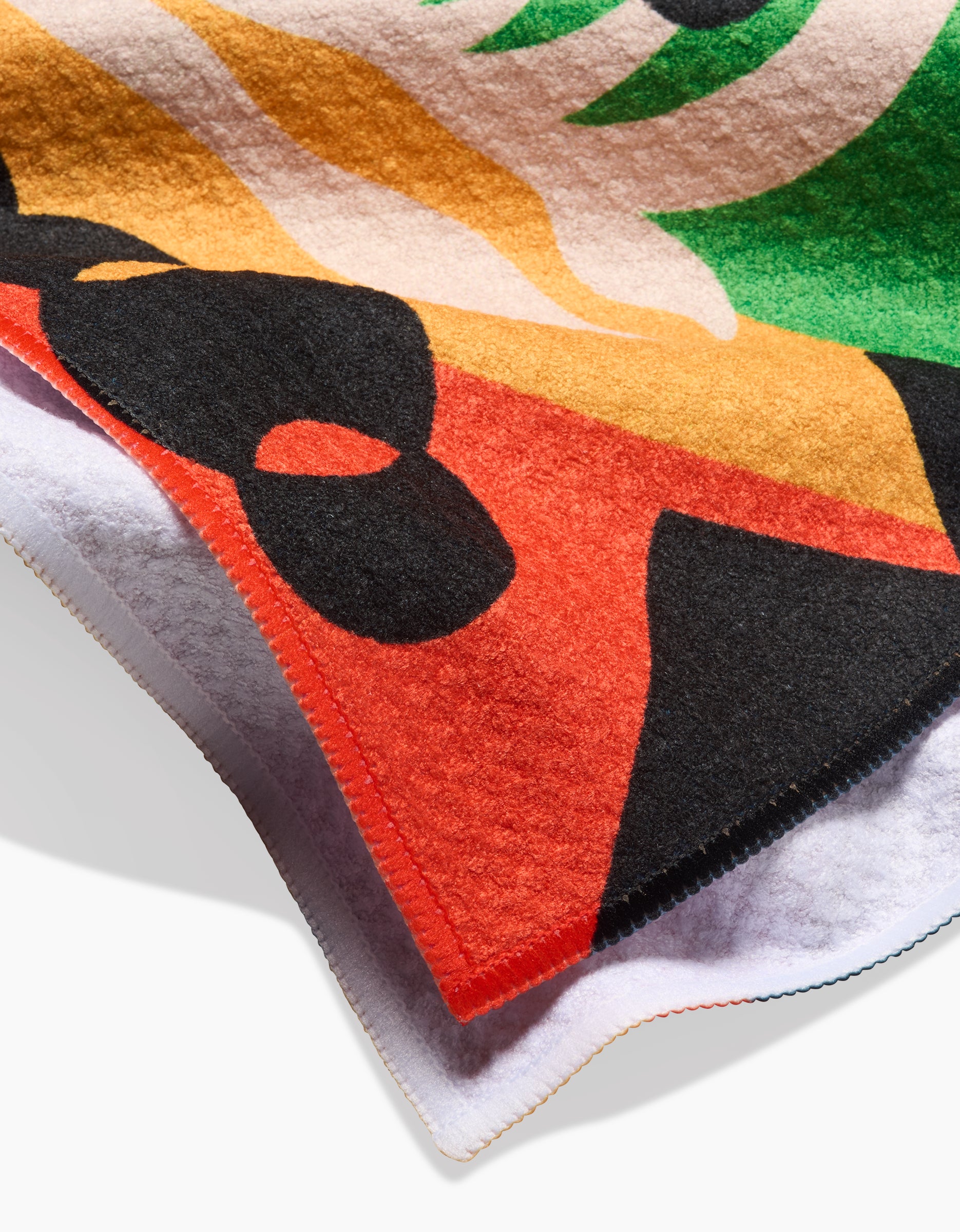 A close-up of the Tamanduá Bandeira fleece by Camila Leão, made with recycled materials. It features bold abstract shapes in black, red, orange, green, and white with stitched edges and overlapping layers.
