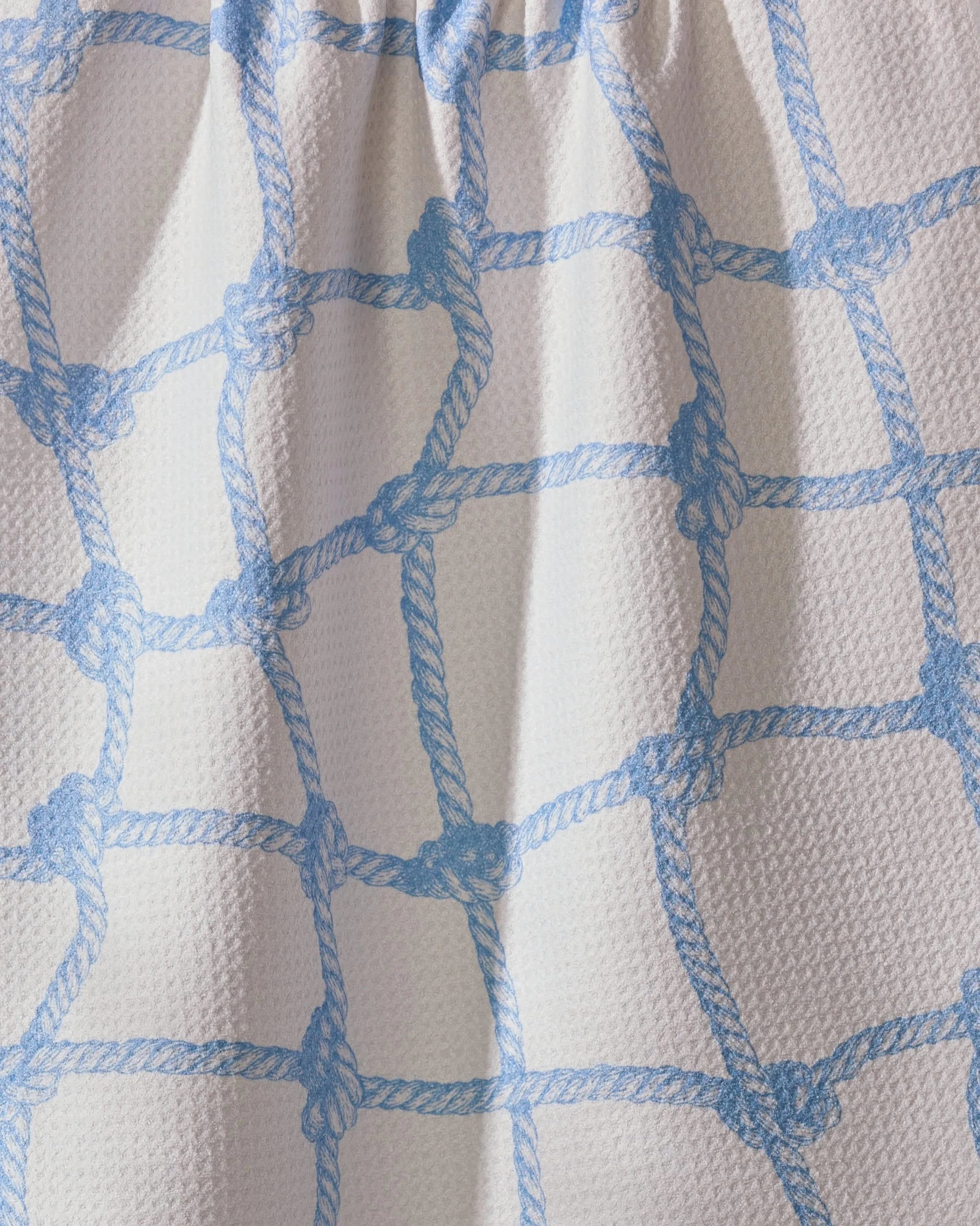 A close-up of Geometry’s Tethered Blue dish towel shows ultra-absorbent white fabric with a light blue rope net pattern, soft folds, and shadows that highlight both its practical design and stylish texture.