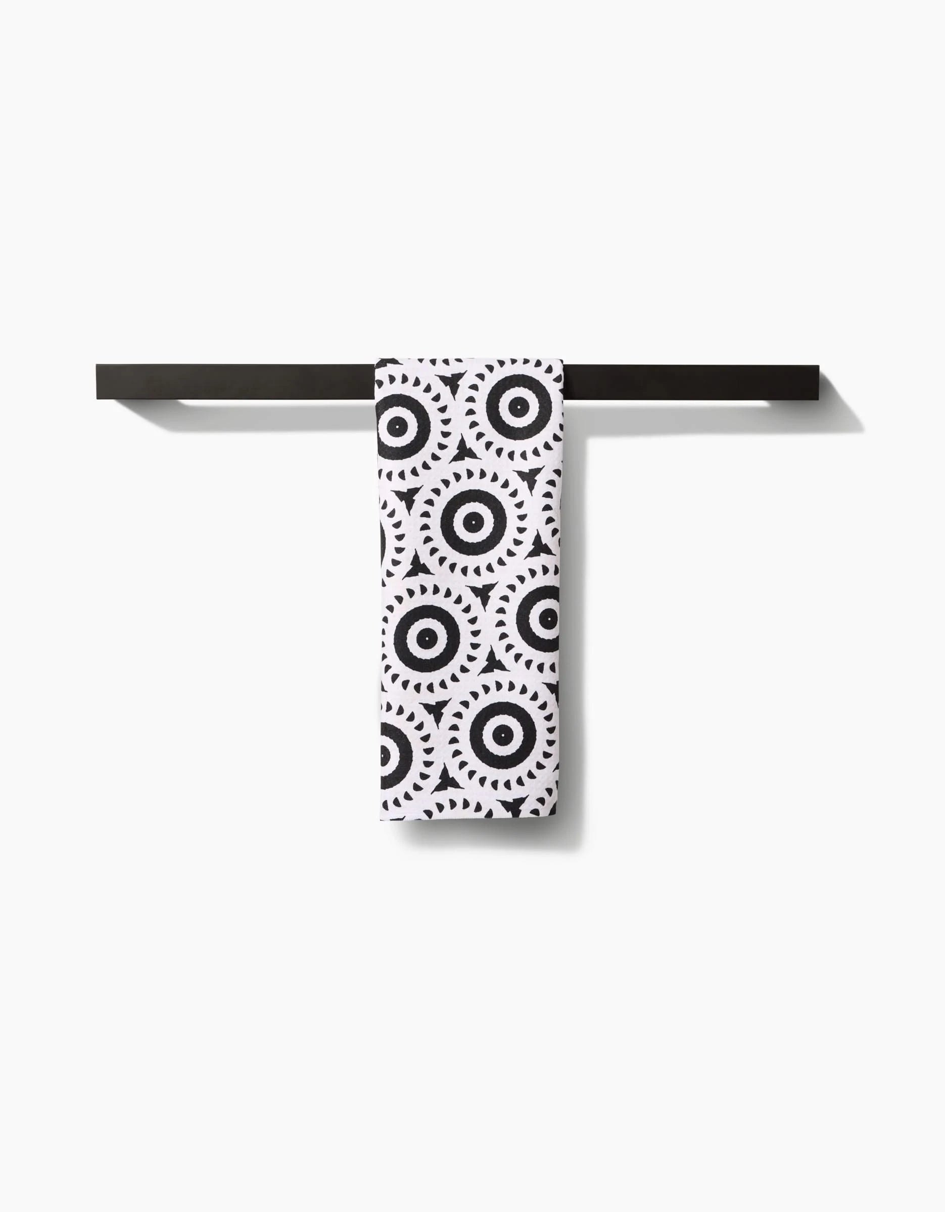 A Katherine Berkeley Texas Two Step tea towel featuring a black circular geometric pattern hangs neatly on a simple, horizontal black towel bar against a plain white background.