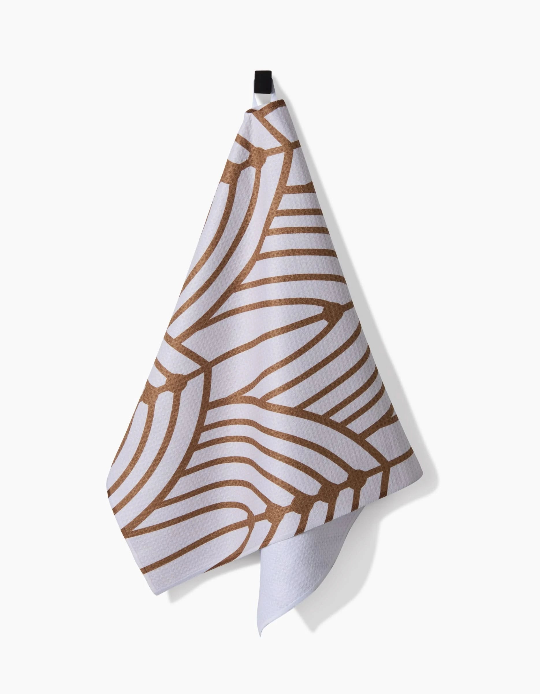 The Amy MacCready Tiffany tea towel, made from post-consumer recycled materials, displays a brown abstract organic line pattern and hangs from a black hook on a plain white background.