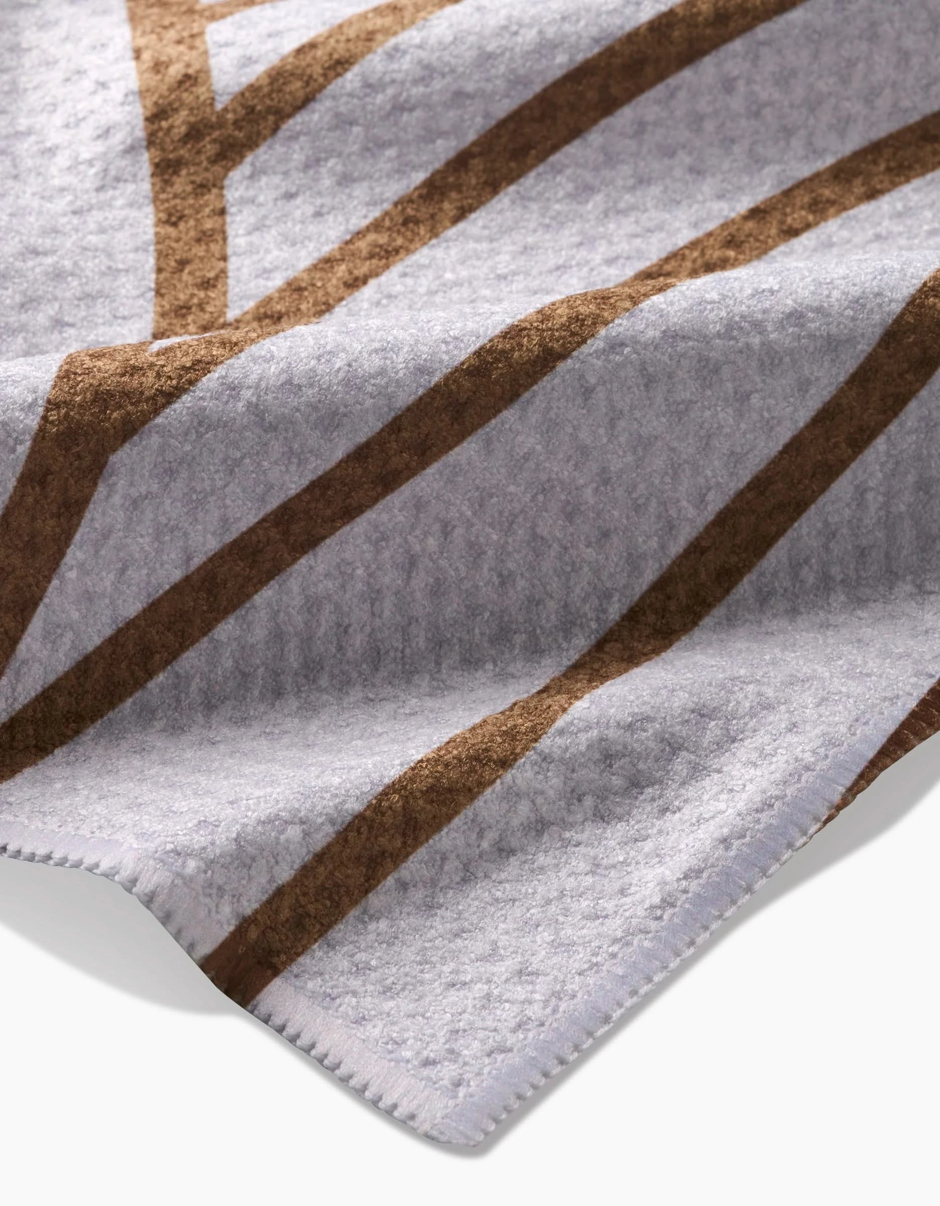 A close-up of the Tiffany blanket by Amy MacCready, made from Geoweave fabric in soft gray with brown geometric lines and detailed edge stitching.