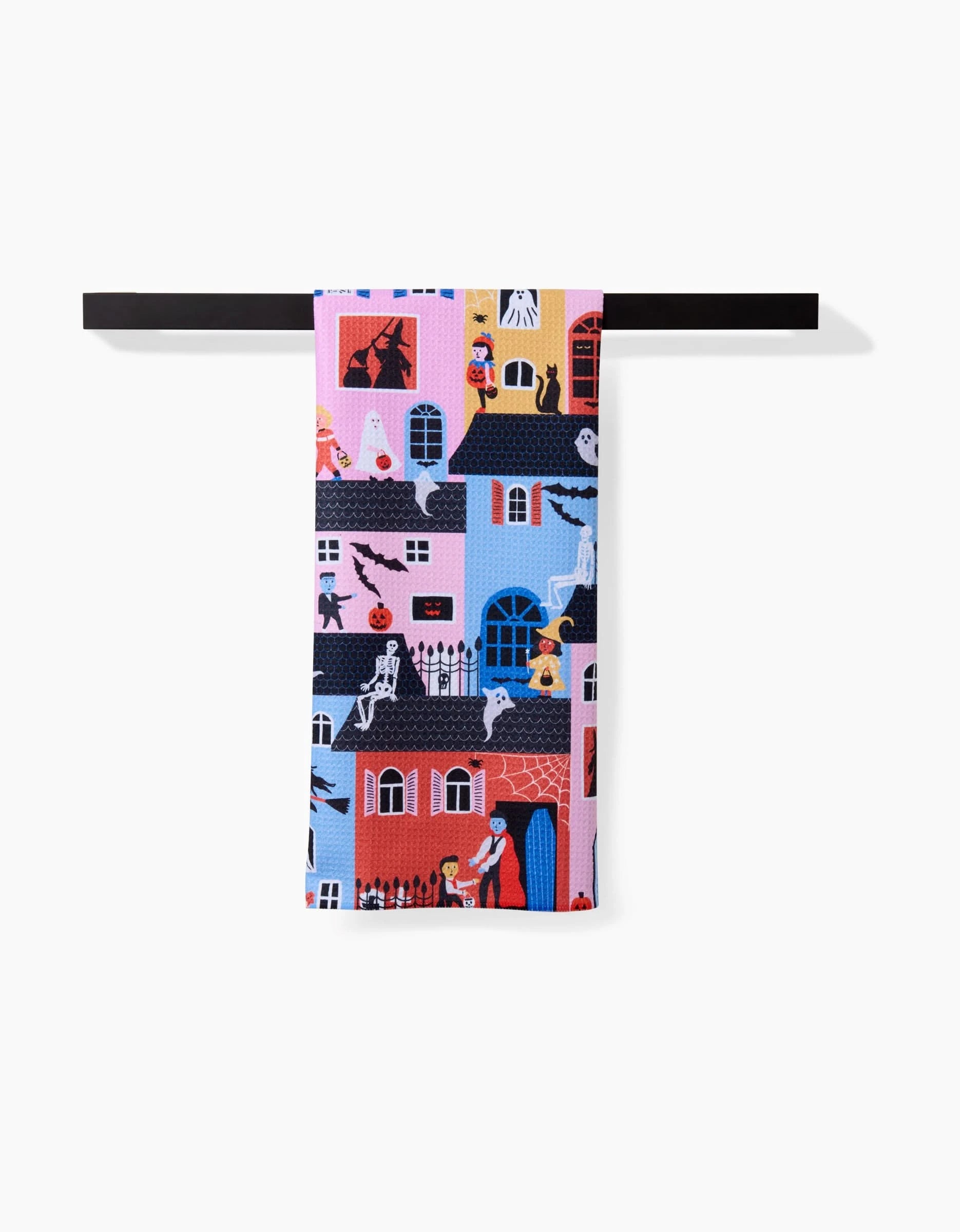 The Trick Or Treat Night tea towel by Ceyda Alasar features a quick-drying, colorful Halloween pattern with haunted houses, ghosts, skeletons, bats, and costumed kids, displayed on a black rod against a white background.