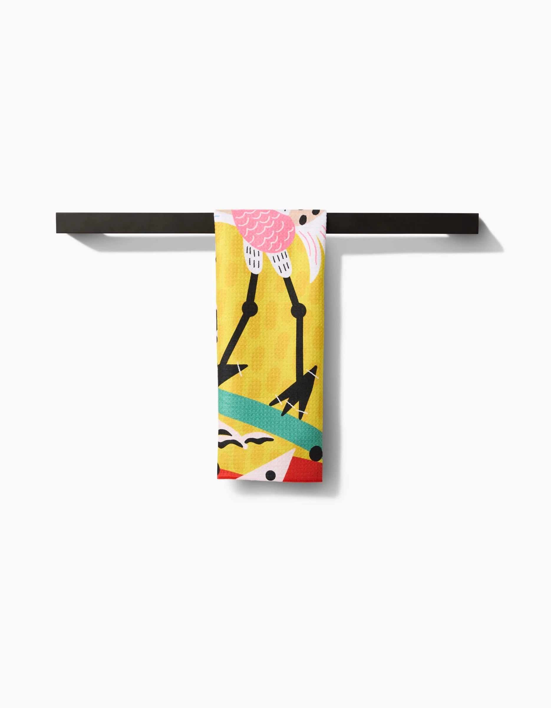 The Tuiuiú tea towel by Camila Leão, featuring a vibrant abstract bird design in pink, yellow, teal, and black, is stylishly displayed on a minimalist black towel bar against a white background.