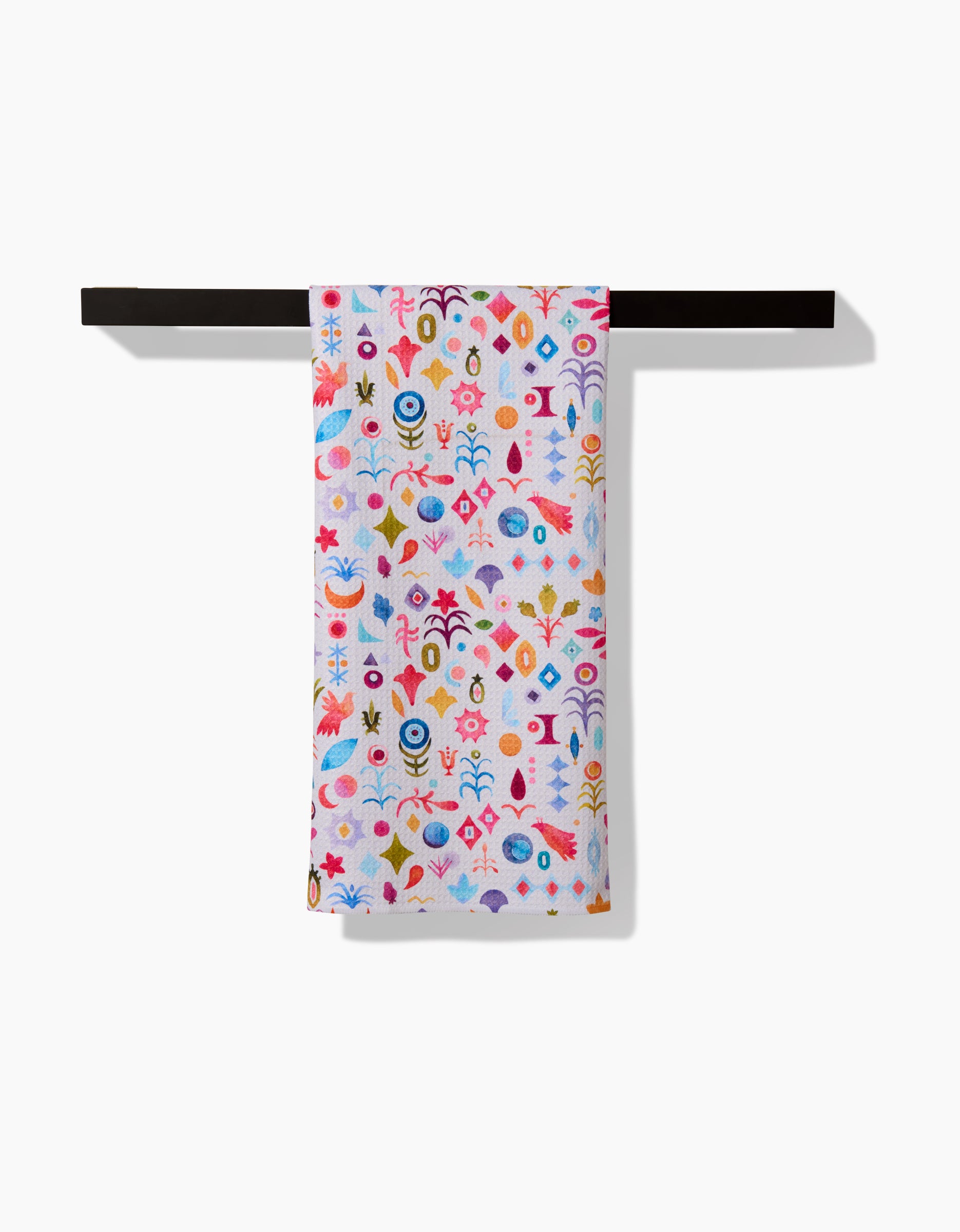 The Tula tea towel by Maayan Alper-Swan, crafted from eco-friendly Geoweave fabric and adorned with vibrant abstract florals and geometric designs, is displayed on a black towel bar against a white background.
