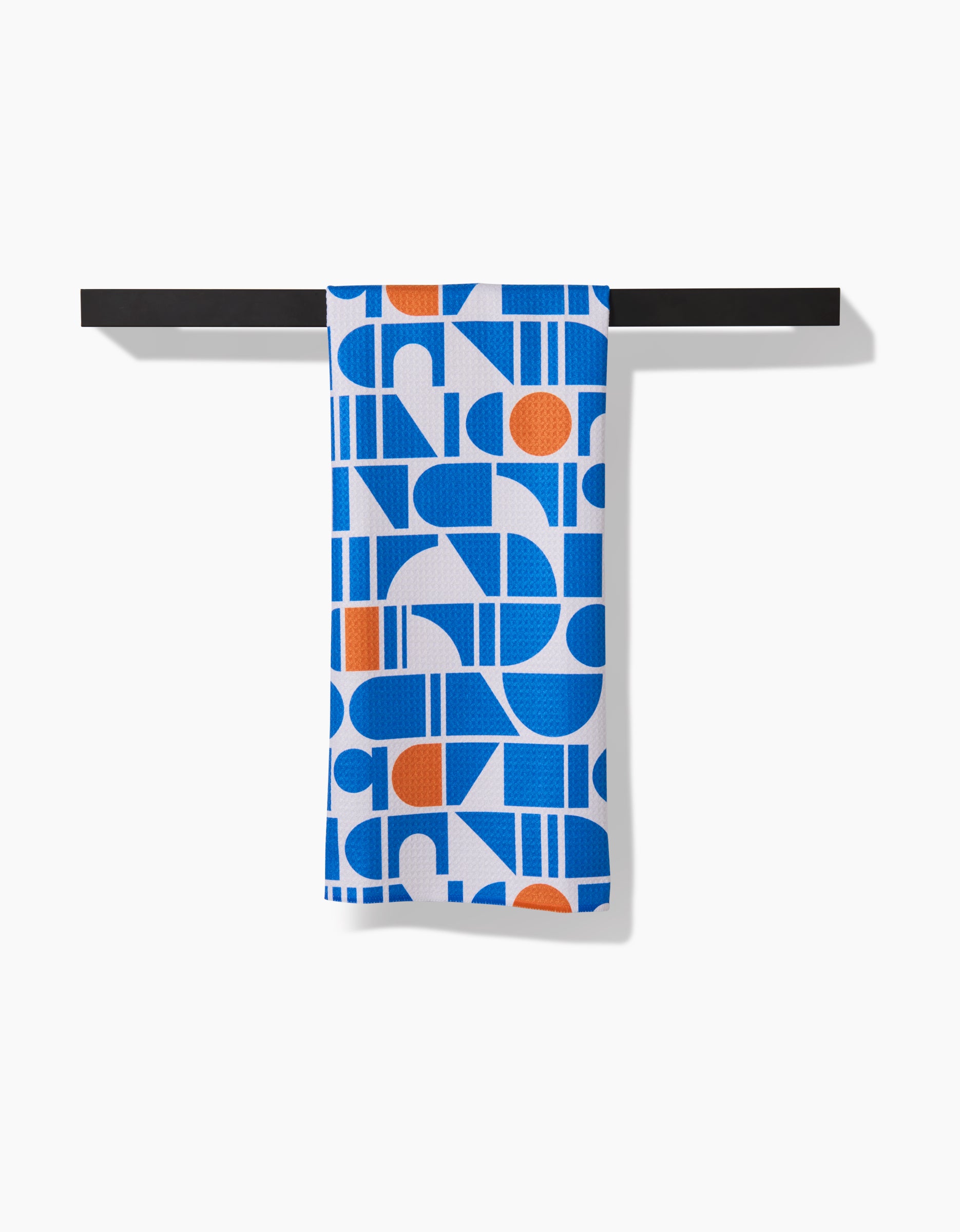 Happy Hemeras Ultra Marine Harmony towel, featuring a bold blue, white, and orange geometric pattern in ultra-absorbent Geoweave fabric, hangs neatly over a black bar against a white background.