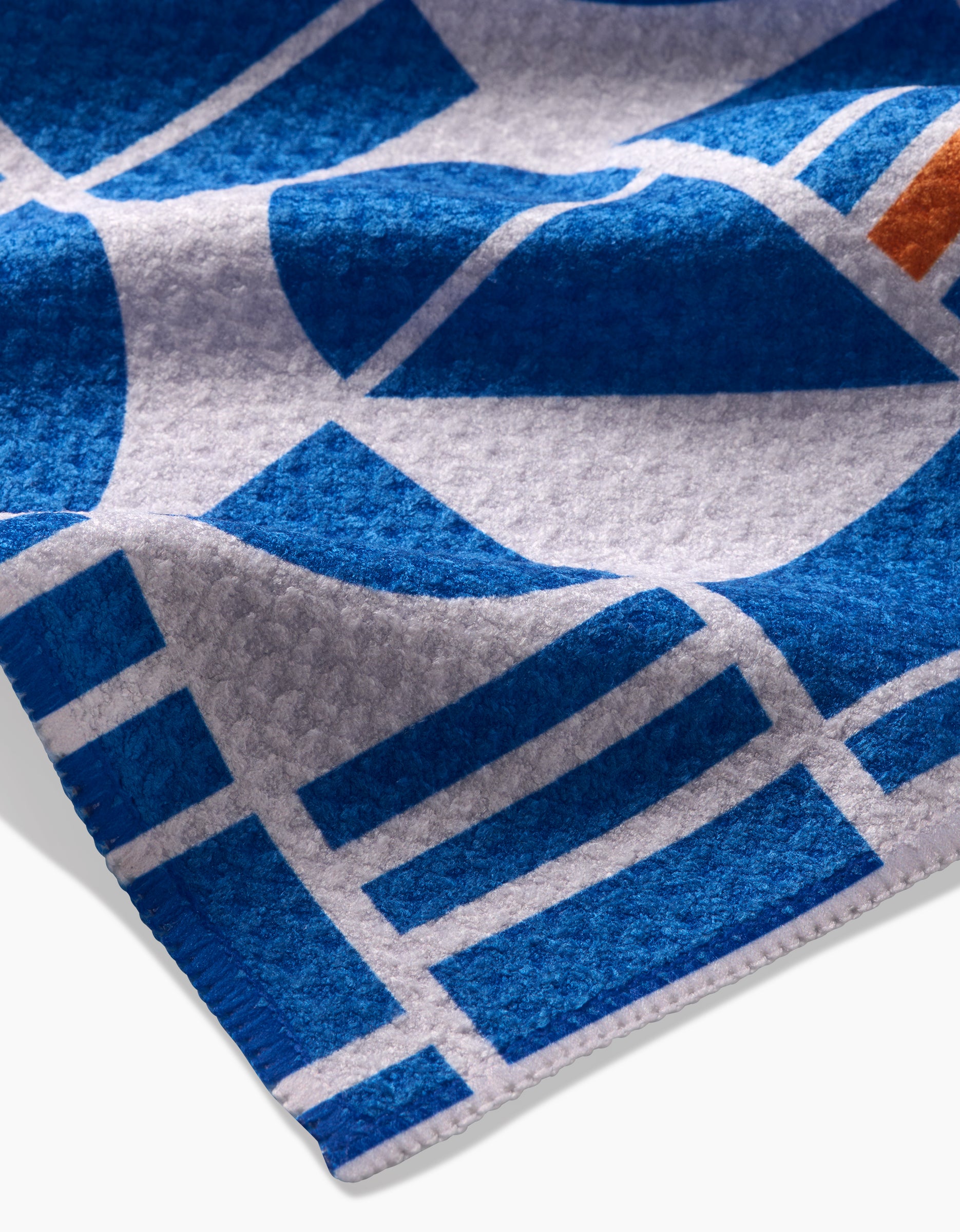 A close-up of Happy Hemera’s Ultra Marine Harmony shows its geometric blue and white Geoweave pattern with an orange accent, clean lines, a soft folded corner, and fabric crafted from recycled materials.