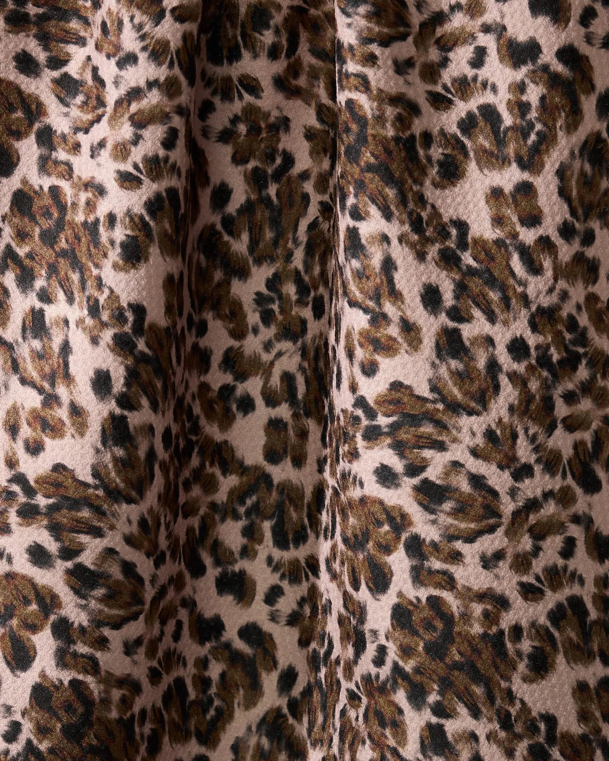 A close-up of Geometrys Umber dish towel, featuring an absorbent fabric with a leopard print in brown, black, and beige. Dark, irregular spots stand out on a light background with visible folds and textured detail.