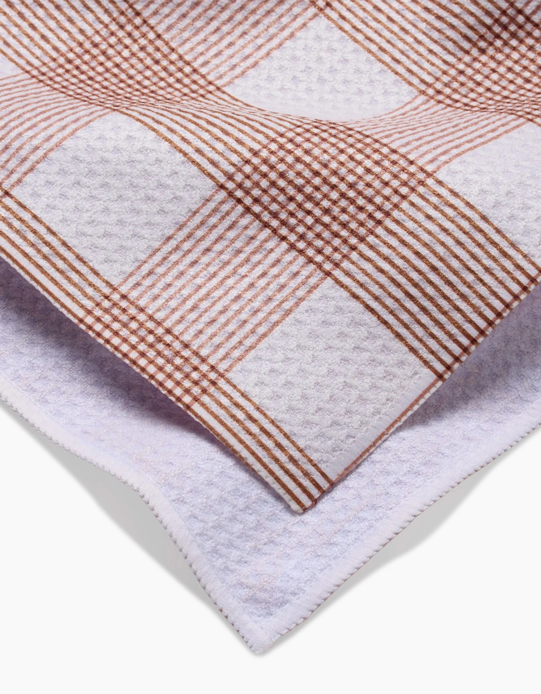 A close-up of Hufton Studios Vintage Gingham Natural tea towel, showing its brown and white checkered front, plain white Geoweave reverse, and neatly stitched edges.