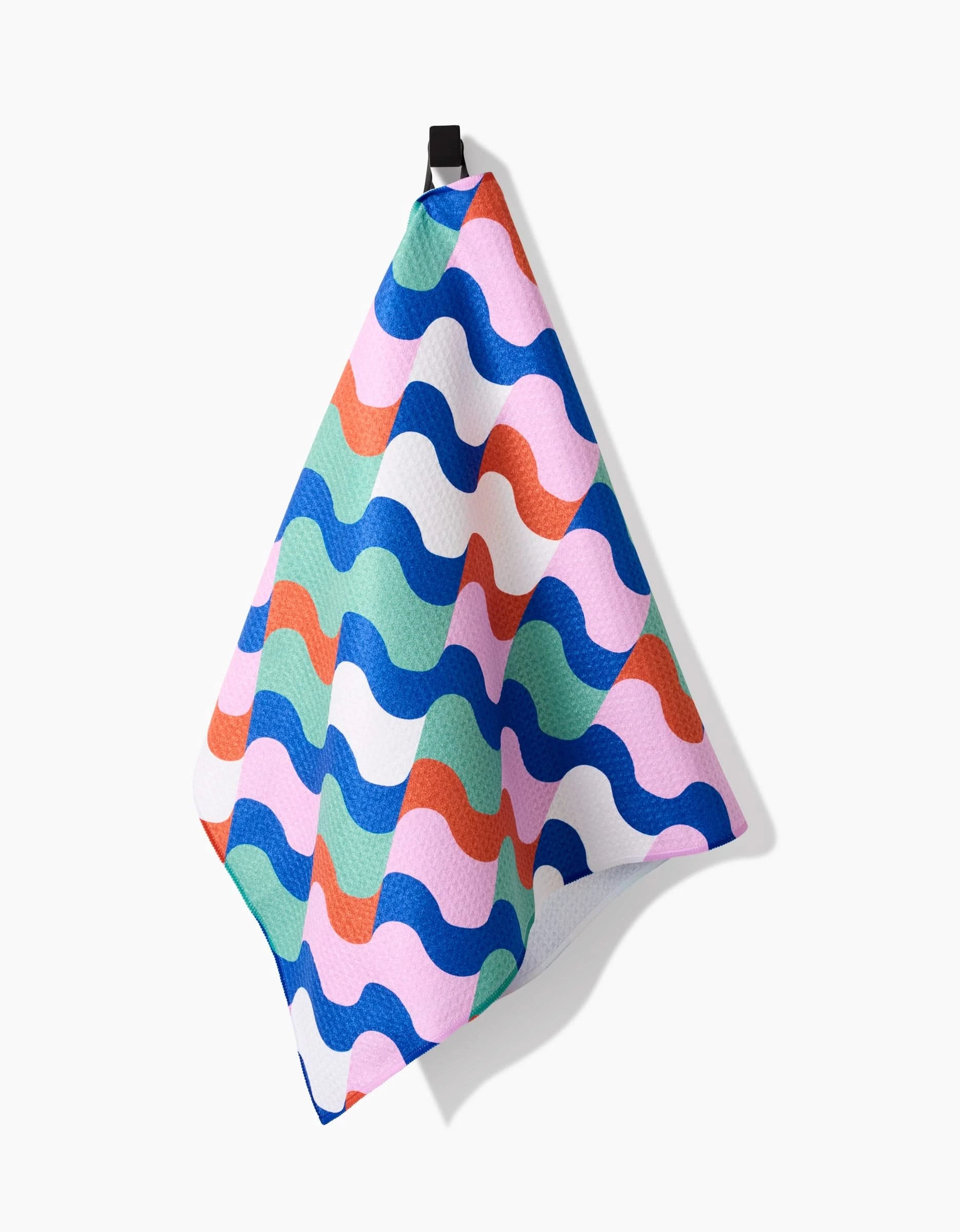 The Wavy Stripes tea towel by Claire Iglesias, made from Geoweave fabric, features colorful blue, green, pink, red, and white waves and hangs from a black loop against a white background.