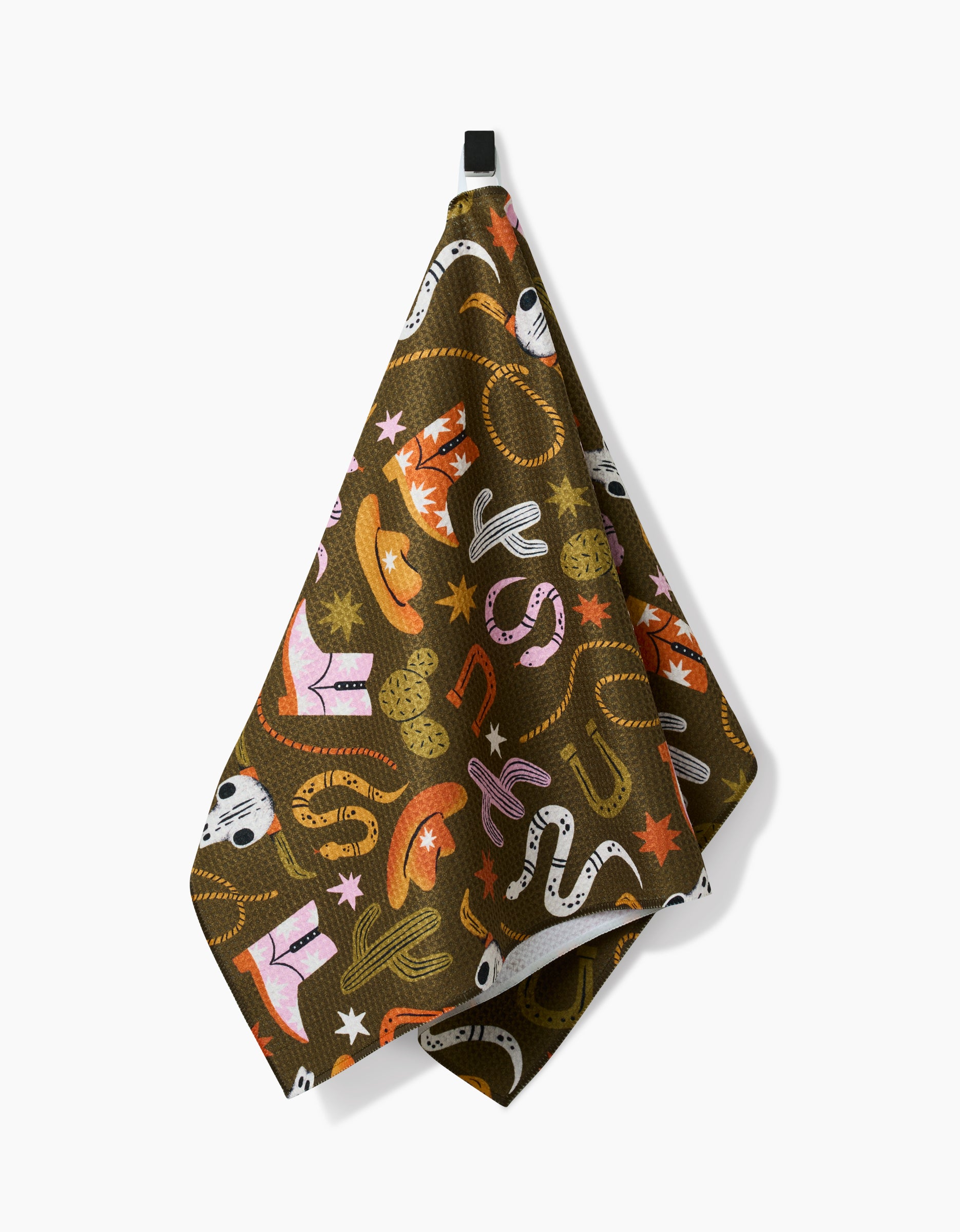 The Megan Roy Wild Cowboy dish towel, crafted from ultra-absorbent Geoweave fabric, displays a vibrant Western pattern of boots, hats, and cacti. It hangs by a black loop against a white background.