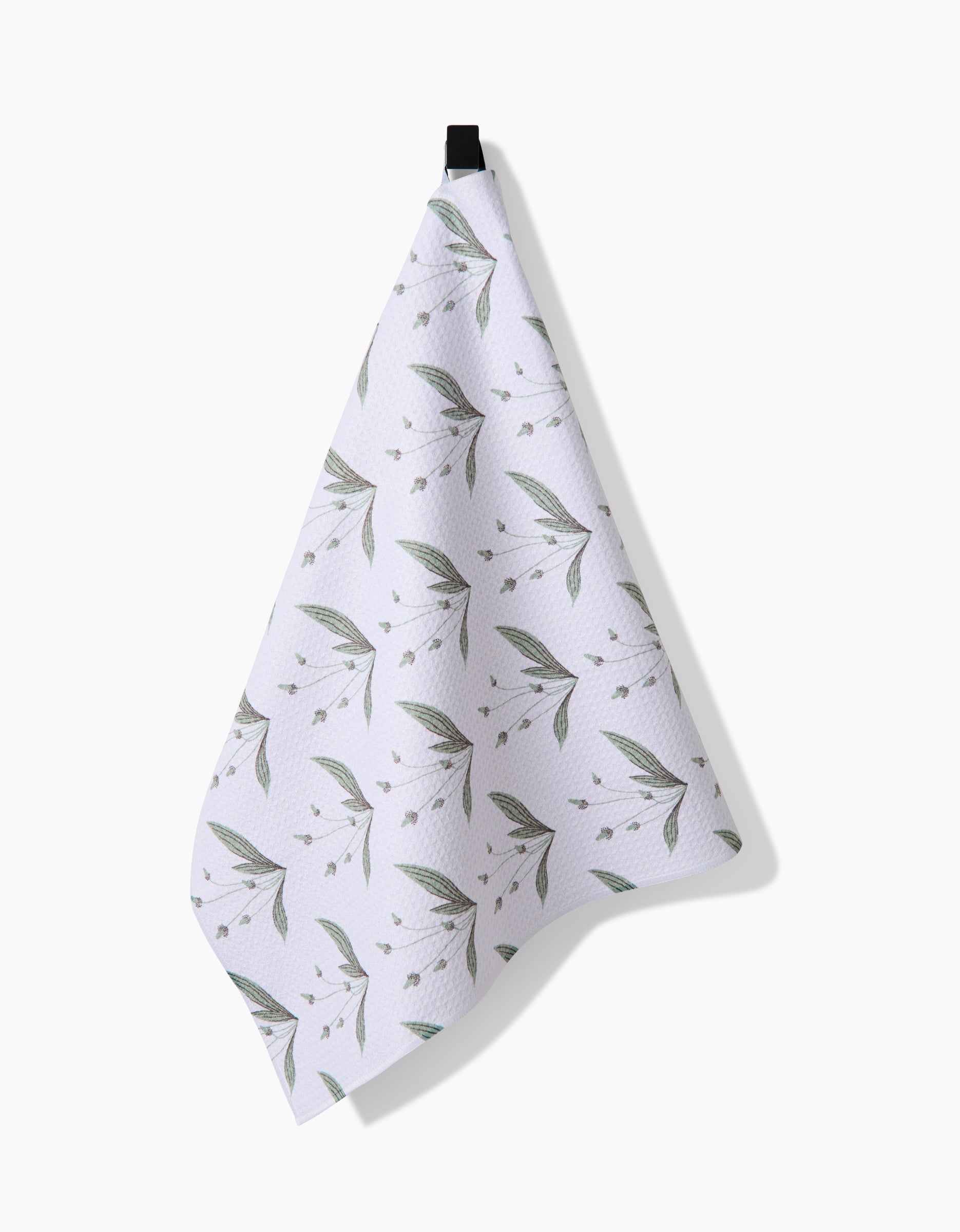 A Linda Fox Wild Leaves Green tea towel, crafted from post-consumer recycled materials and featuring a subtle leafy pattern, hangs by a black loop against a plain white background.