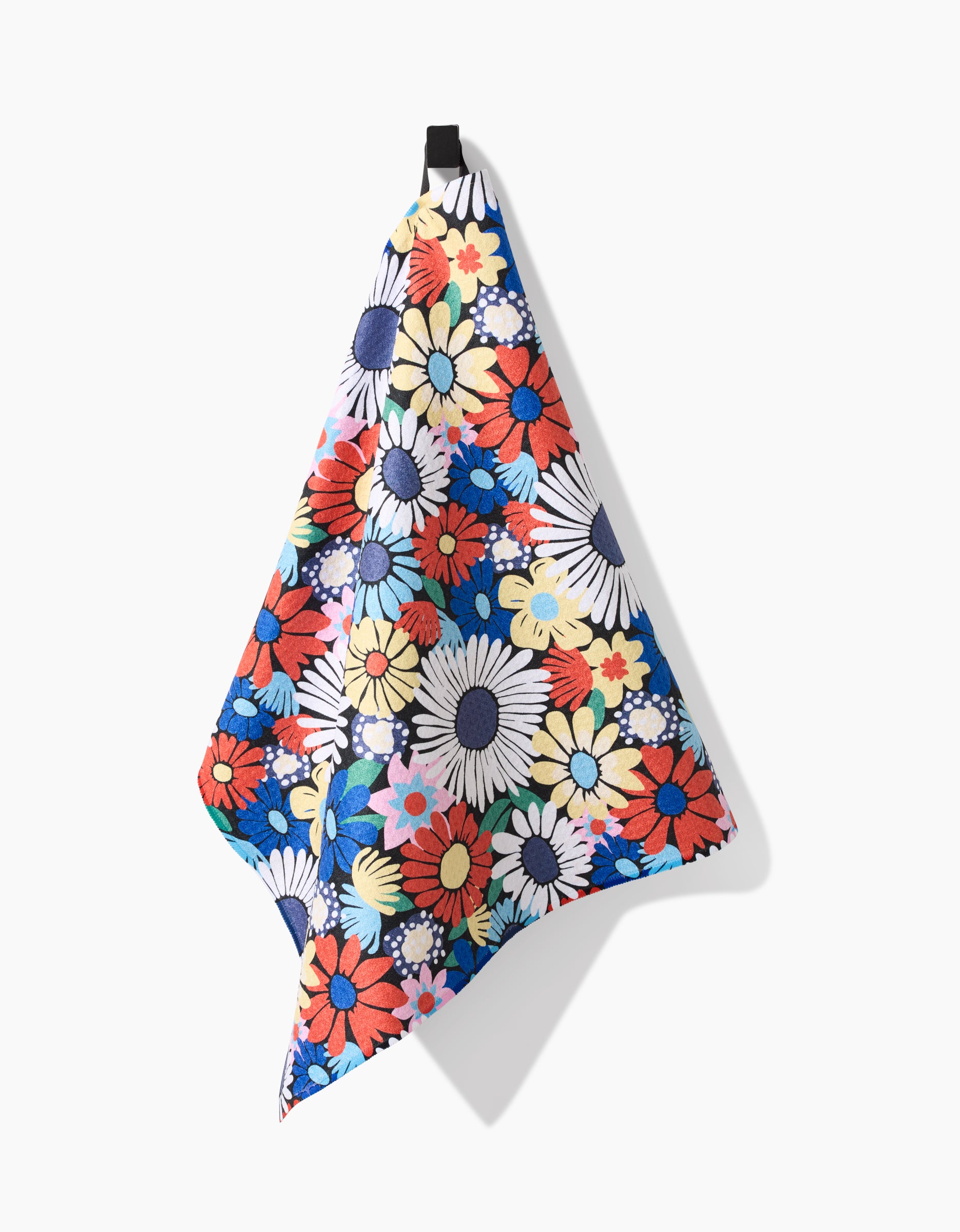 The Claire Iglesias Wildflowers Bouquet tea towel features a vibrant floral Geoweave™ fabric with large daisies and other flowers in red, blue, yellow, white, and pink, hanging from a black loop against a white background.