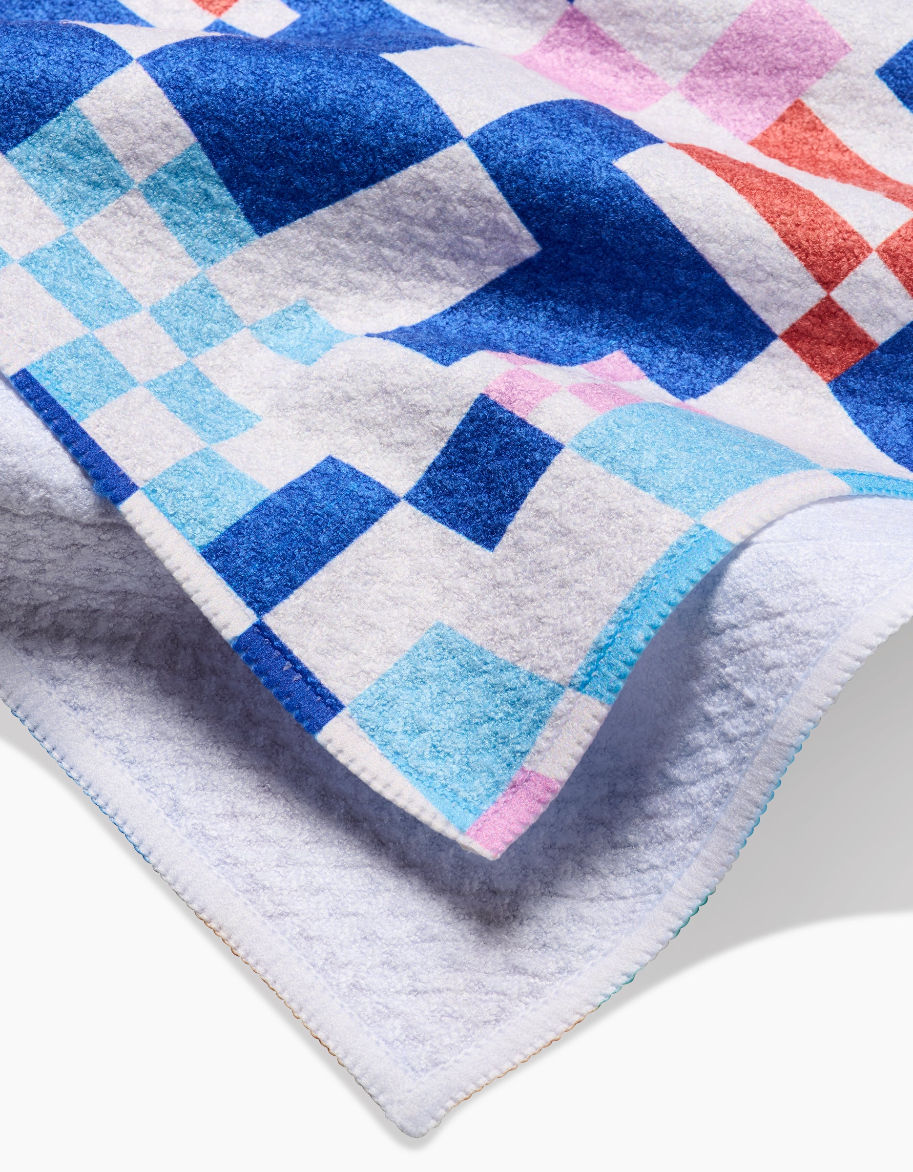 A close-up of the Claire Iglesias Wonky Checkers tea towel, showing its soft Geoweave fabric and detailed stitching with a colorful geometric pattern of blue, pink, red, and white squares.