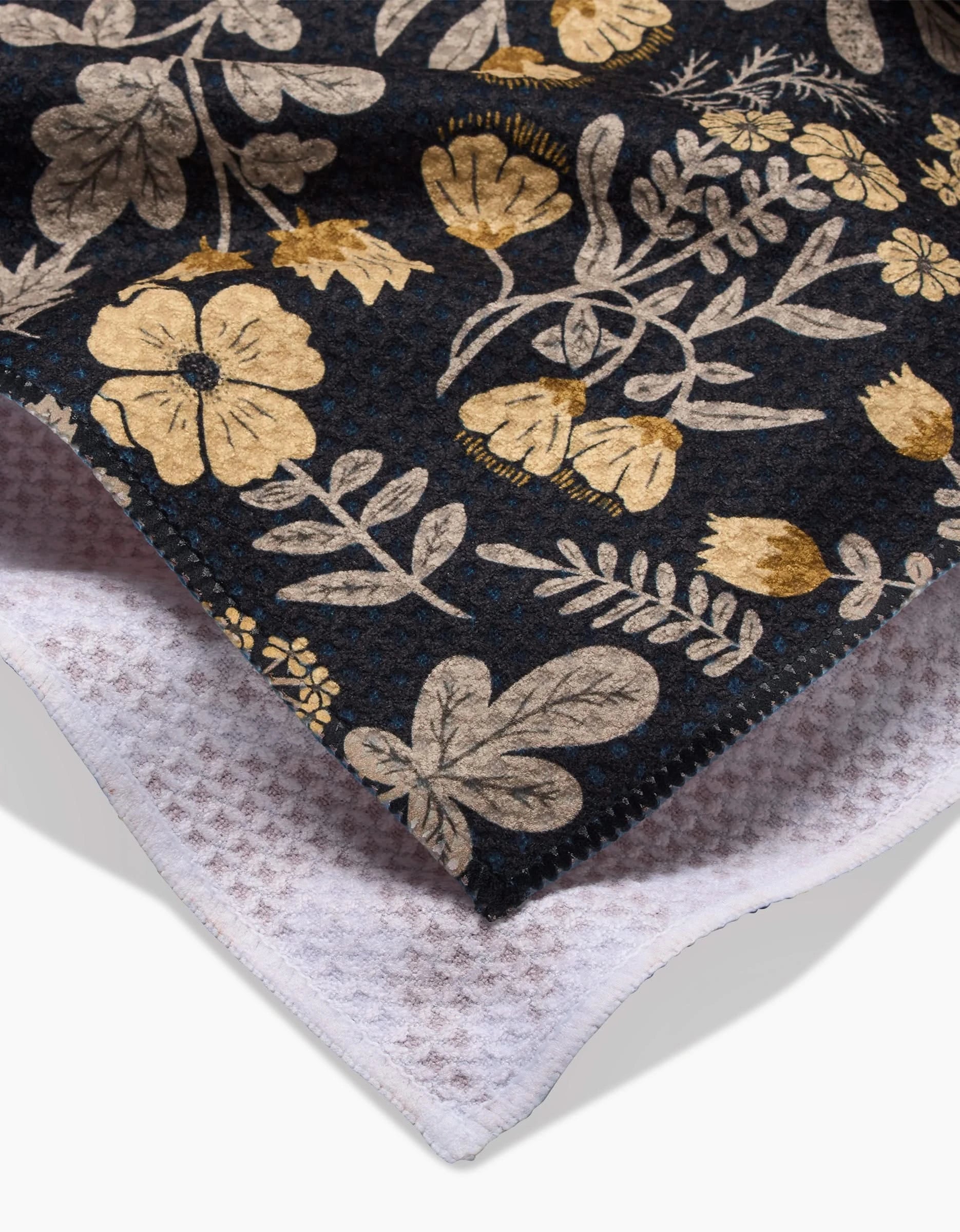 A close-up of Danelys Sidrons Woodland Wildflowers: a dark fabric with gold and beige floral patterns, layered over an ultra-absorbent white waffle-knit tea towel.