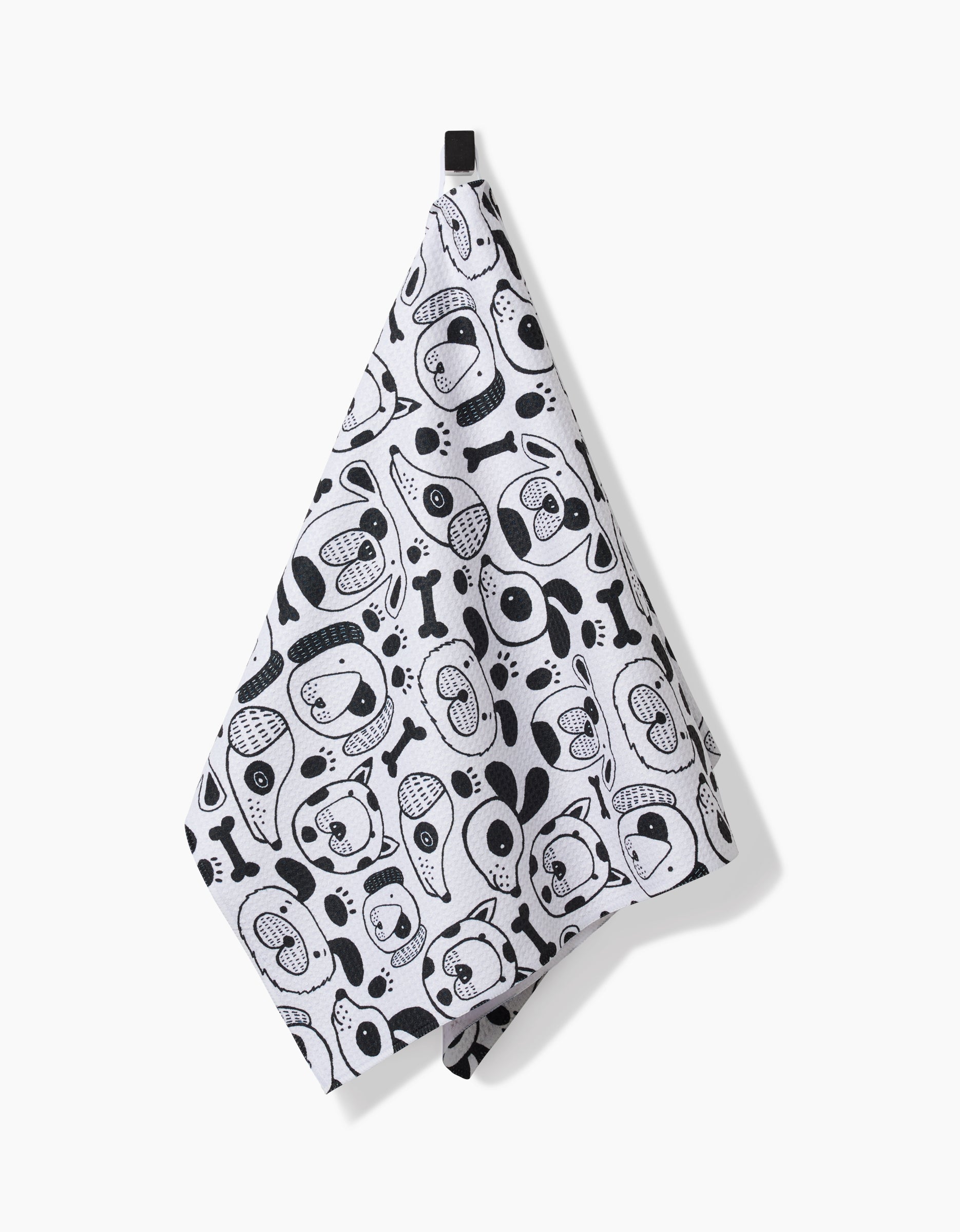 The Woofin Around kitchen towel by Jessica Swift, made from ultra-absorbent Geoweave fabric, features black cartoon dog faces and bones on white and hangs from a black loop against a white background.