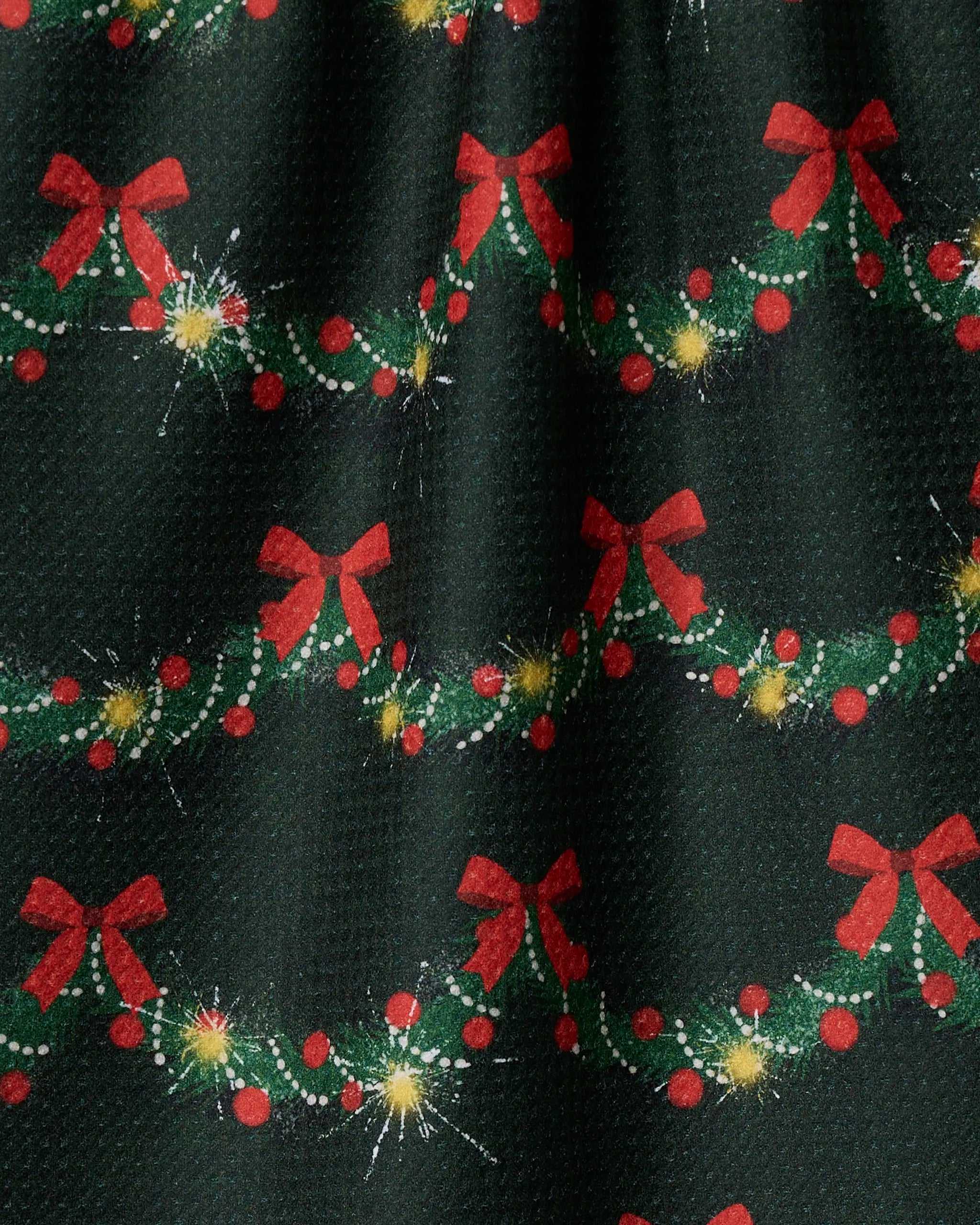 The Geometry Yuletide Garland kitchen towel features a festive pattern of green garlands, red bows, berries, and yellow stars on a dark background. Made from ultra-absorbent fabric, it adds holiday cheer to your kitchen.