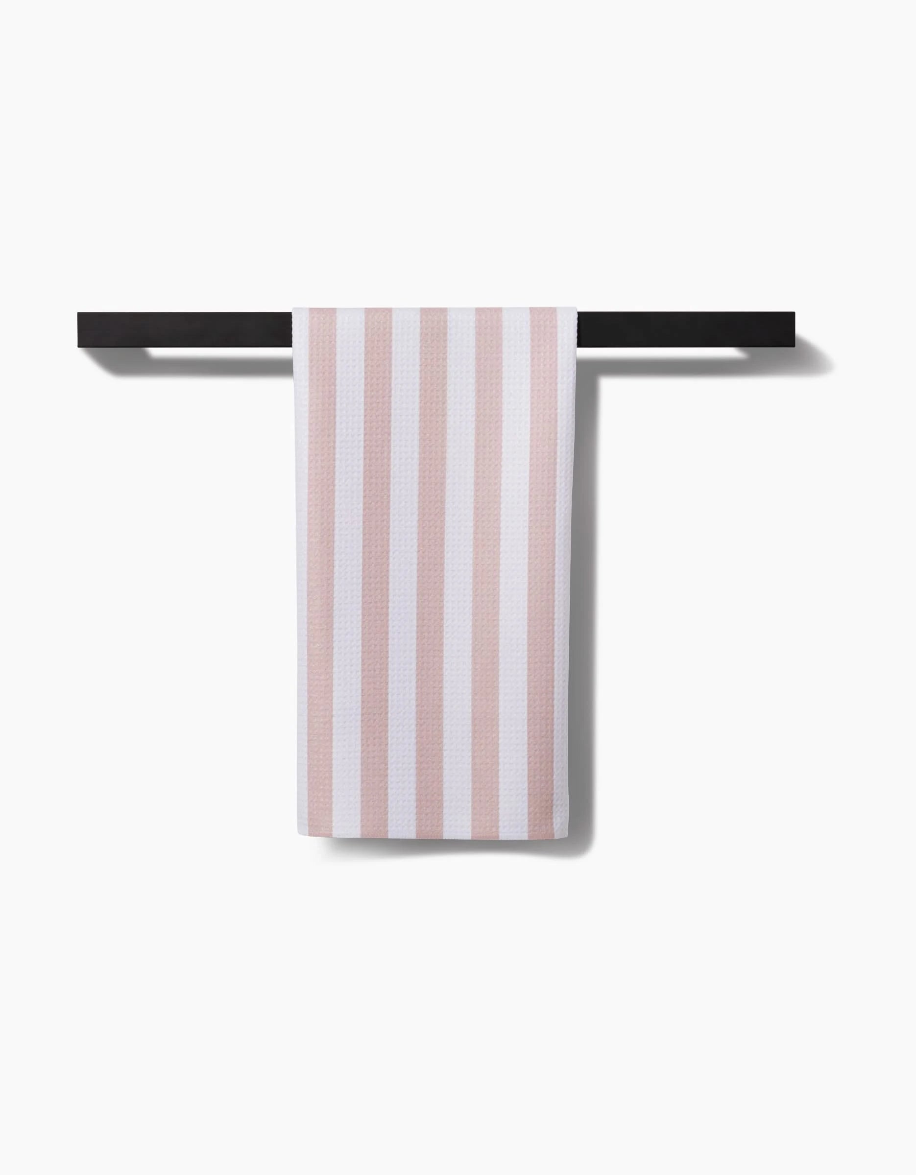 The Kailee Wright Yvonne Stripe tea towel, featuring pink and white stripes, hangs neatly on a sleek black towel bar against a white background.