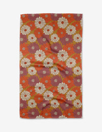 The Zinnia Forever tea towel by Kayla Ann features a retro floral design with bold white, orange, red, and olive green flowers on a reddish-purple background. Made from recycled materials, the fabric may display slight wrinkles.