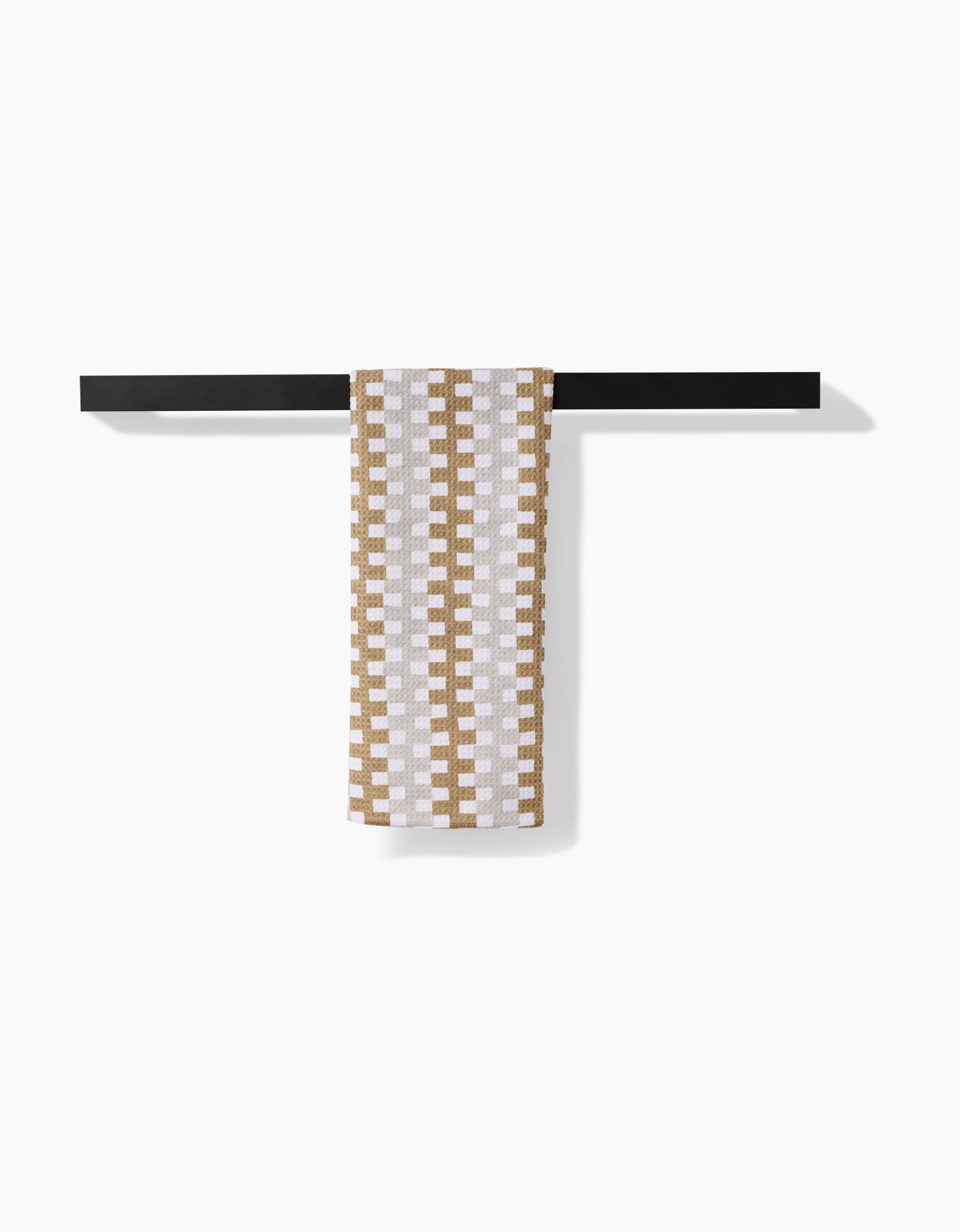 The Zippy recycled kitchen towel by Studio Jeannot, featuring a brown geometric checkered design on white, hangs neatly over a minimalist black bar against a plain white backdrop.