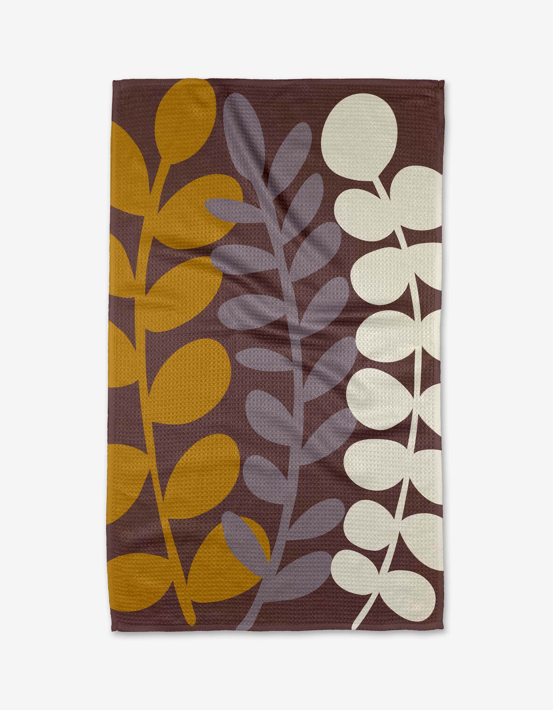 The Three Branches tea towel by Lizzie Clark is rectangular and made from recycled materials, showcasing a brown background with three large vertical leaf patterns in mustard yellow, light purple, and off-white.
