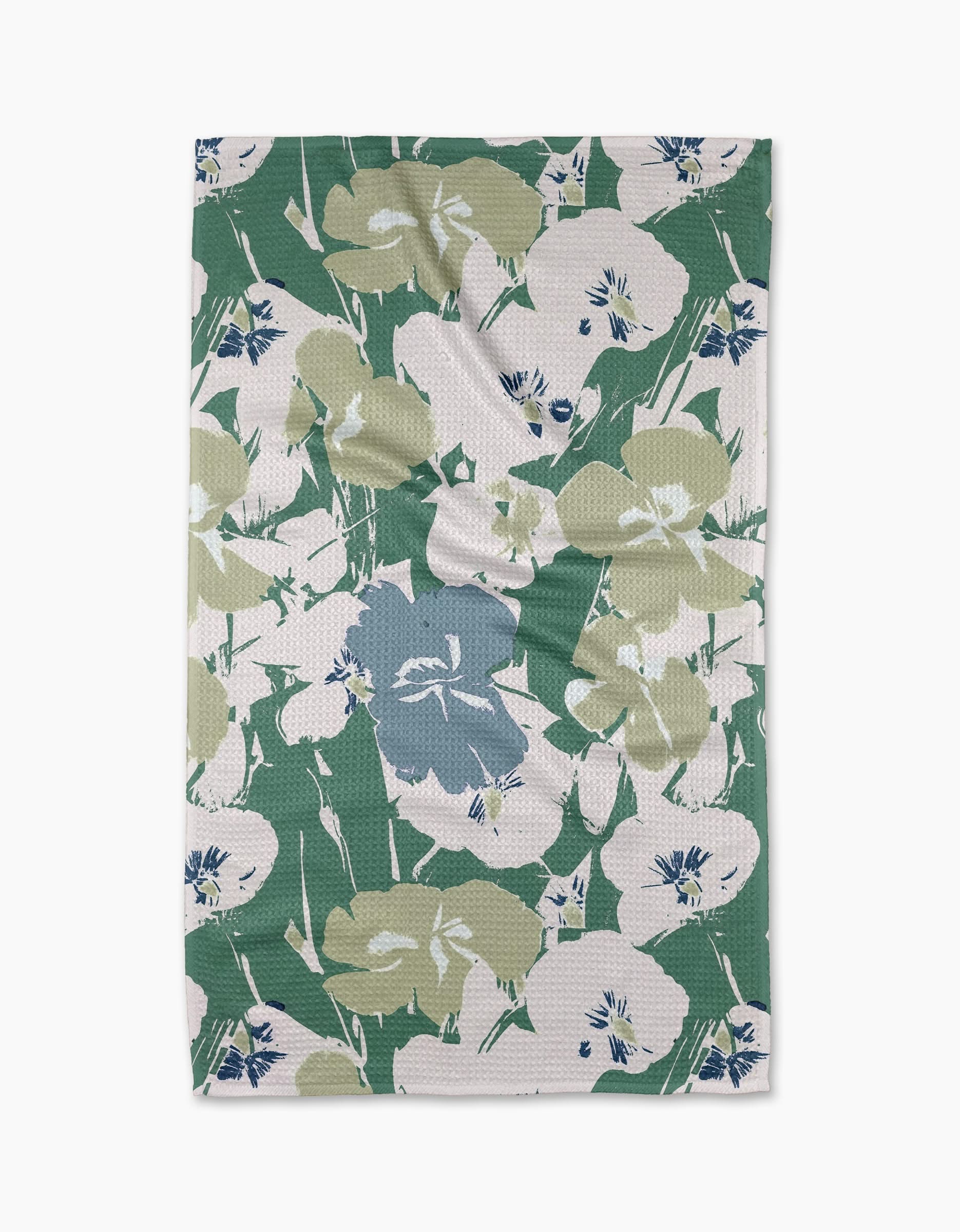 The Geometry Brie tea towel is rectangular and features a floral pattern with large green, blue, and white flowers and leaves on a white background. The cloth may display minor wrinkles.