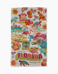 The Geometry Greetings From Florida tea towel is ultra-absorbent and colorful, featuring Florida icons like flamingos, oranges, palm trees, alligator, sea turtle, sun, beach scenes, and “Greetings from FLORIDA The Sunshine State” text.
