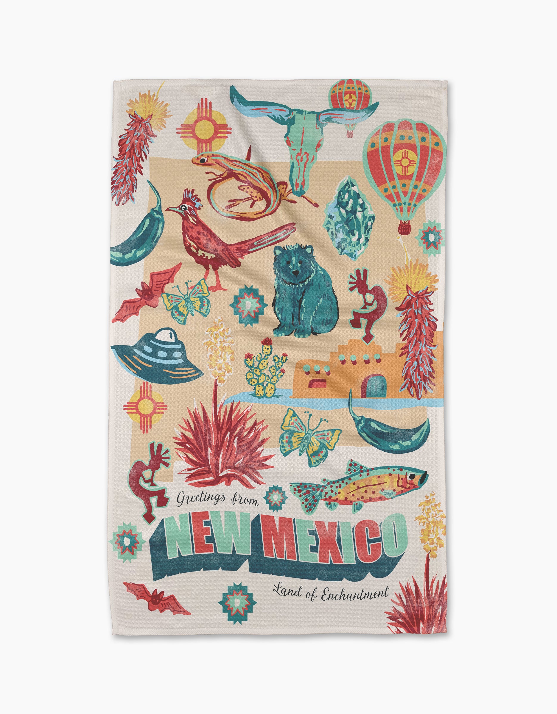 Geometry's "Greetings From New Mexico" tea towel features vibrant illustrations—including a chili pepper, hot air balloon, roadrunner, cactus, UFO, skull, bear, and pottery—on recycled material with “Land of Enchantment” text.
