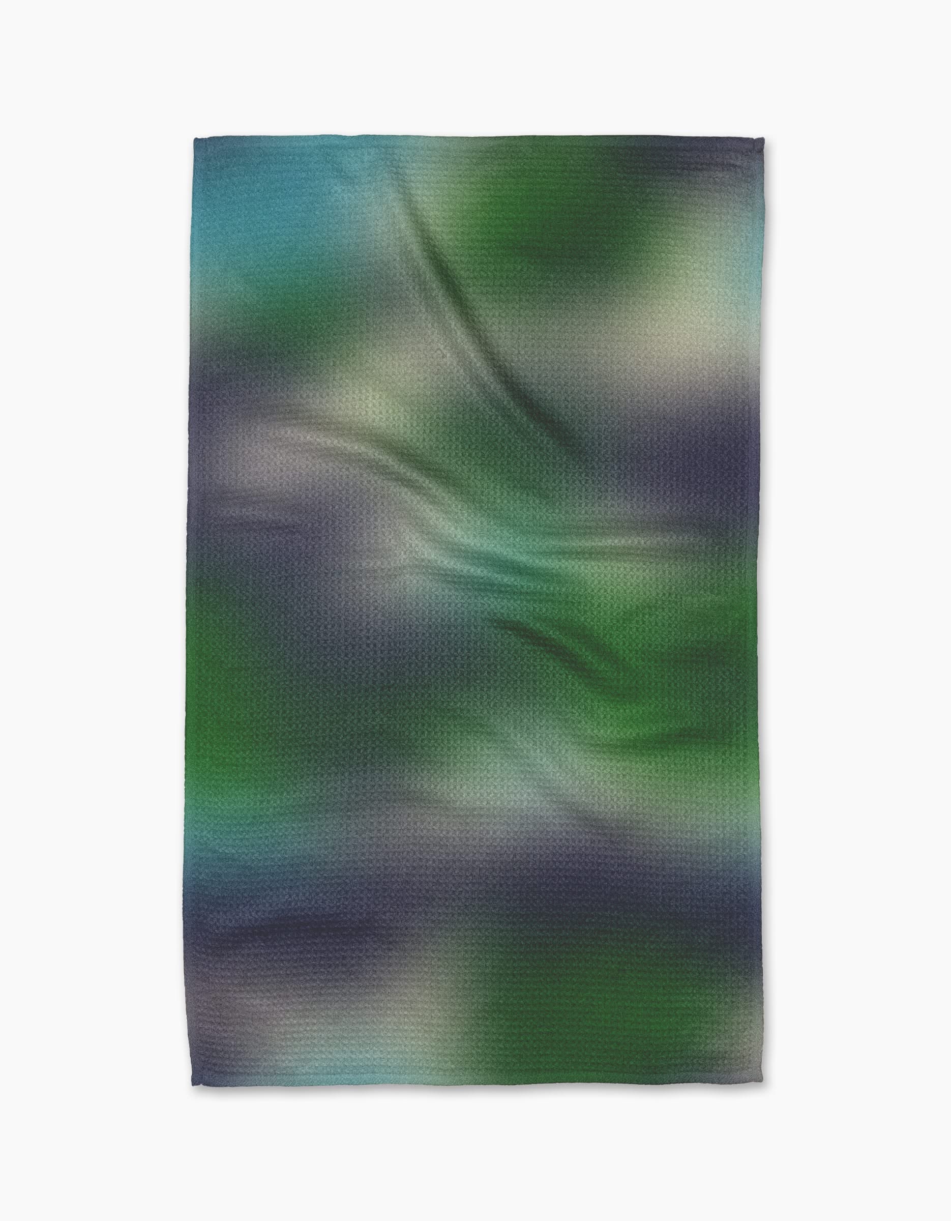 The Geometry Haze Kitchen Tea Towel features a blurred gradient in blue, green, black, and white. Made from recycled materials, this ultra-absorbent towel lays flat on a white background with subtle creases.