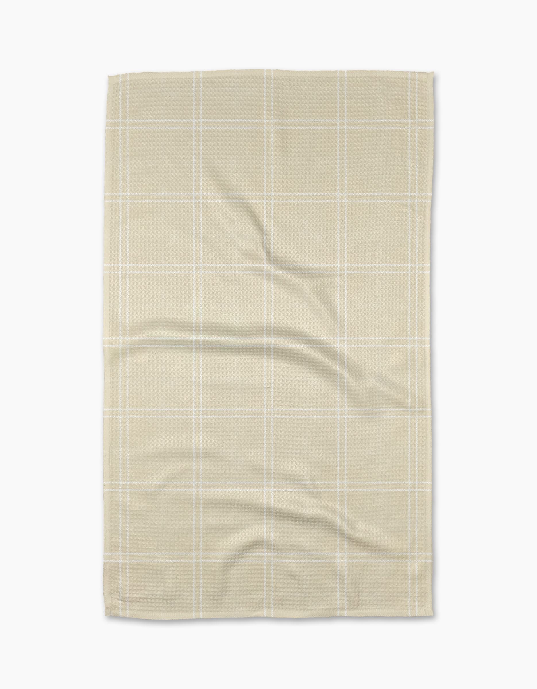 The Geometry Hearth Oat tea towel features a subtle white checkered pattern on beige recycled fabric, displayed flat with soft folds and creases against a white background.
