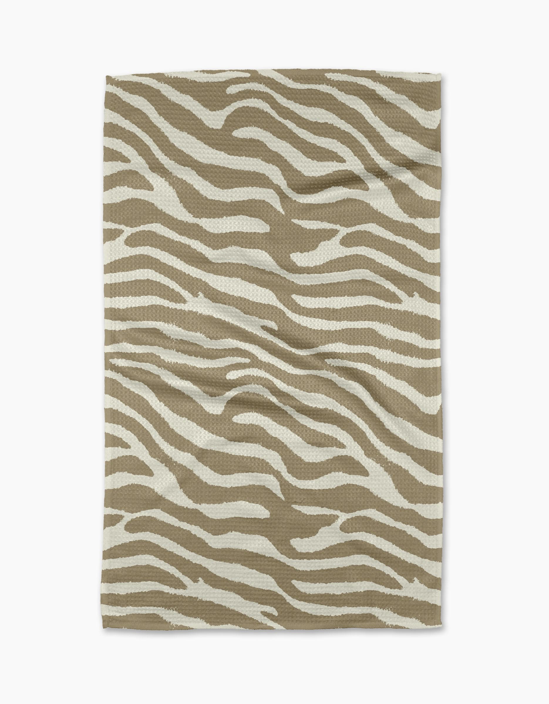 The Zira Tan tea towel by Geometry features a white zebra stripe pattern on rectangular beige fabric, displayed flat on a white background.