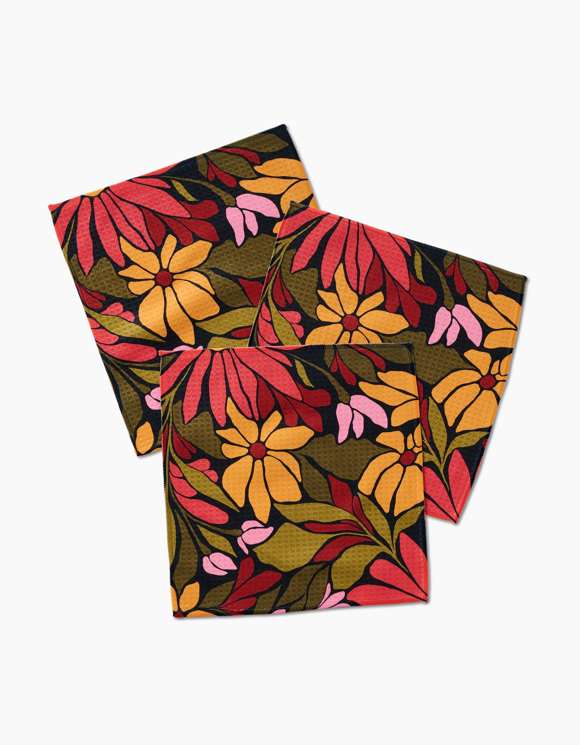 Three folded GEOMETRY Luxe Washcloths in the Blooming Black design, showcasing bold red, yellow, and pink flowers with green leaves on a dark background, made with ultra-absorbent Geoweave technology.