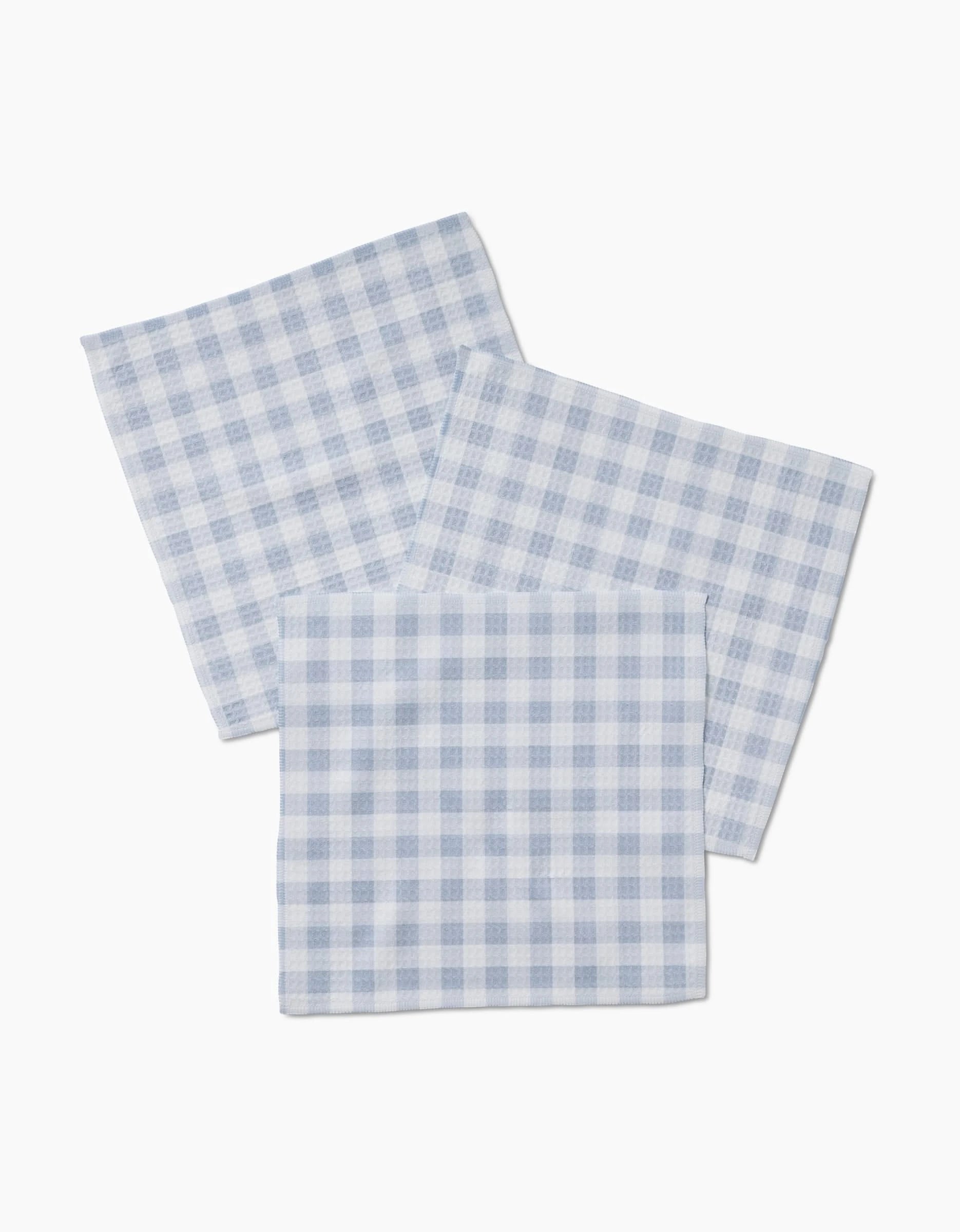 Three Aubrey Fairchild Blue Gingham cloth napkins, made with ultra-absorbent Geoweave technology, overlap each other on a white background.